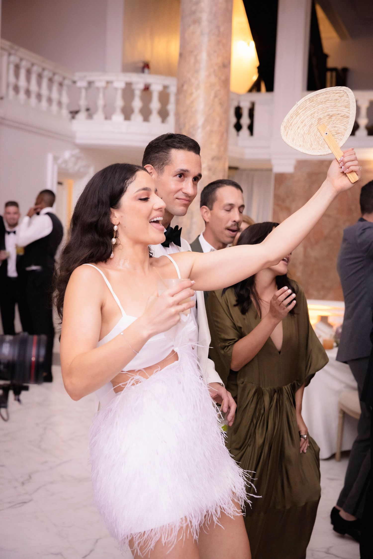 Wedding reception scene with dancers enjoying an energetic moment in an elegant ballroom with marble columns and chandeliers.