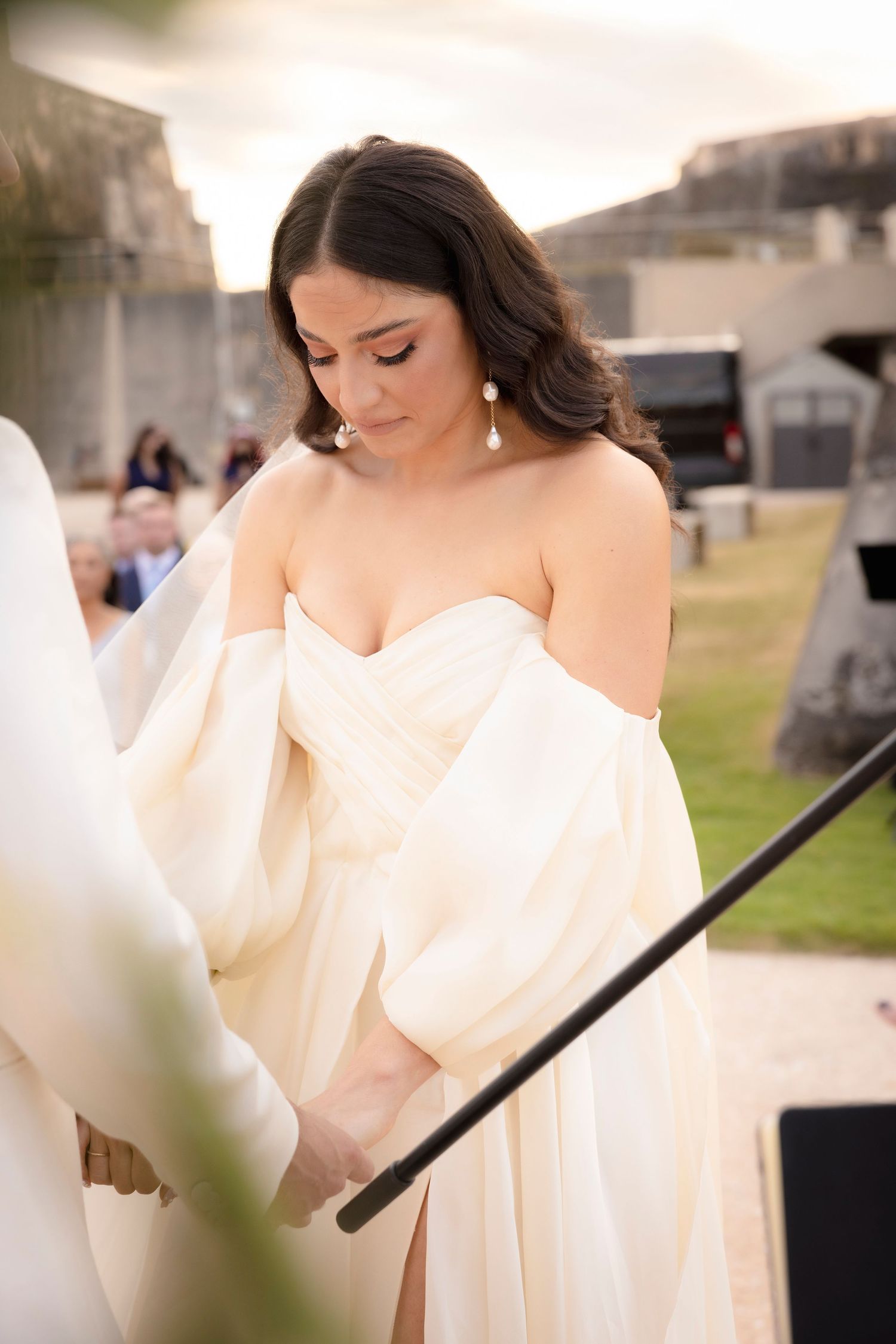 Elegant bride in flowing white dress photographed outdoors against stone architecture.