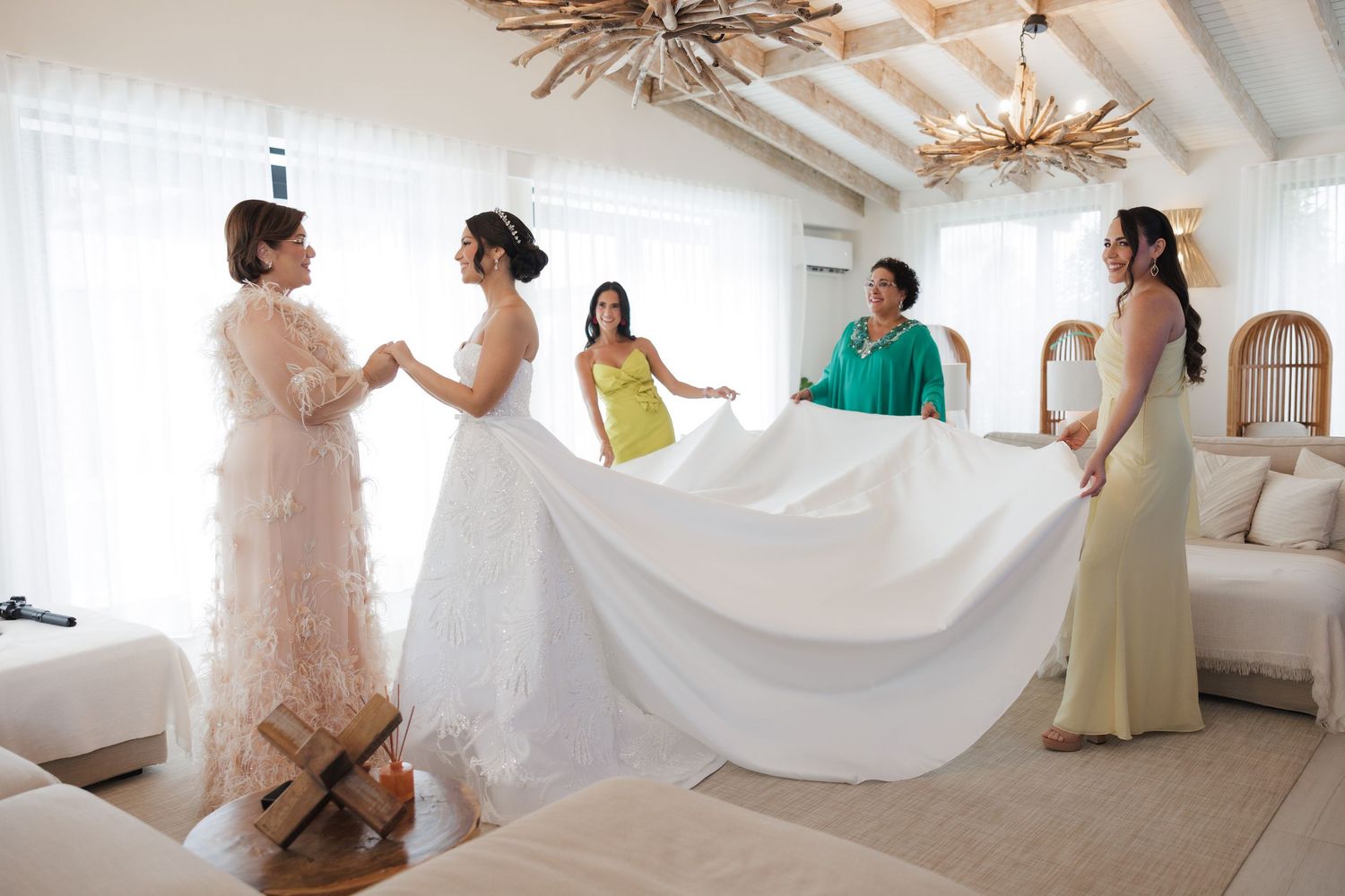 Bridesmaids in light colored dresses gather in a bright white room with vaulted ceilings.