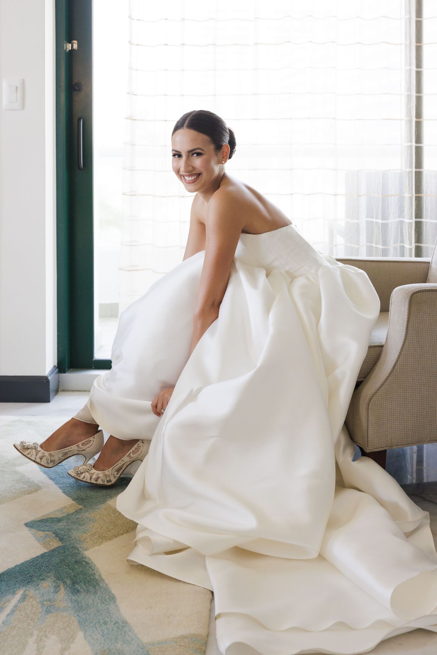 Bride in elegant white gown sitting gracefully on floor with decorative shoes.