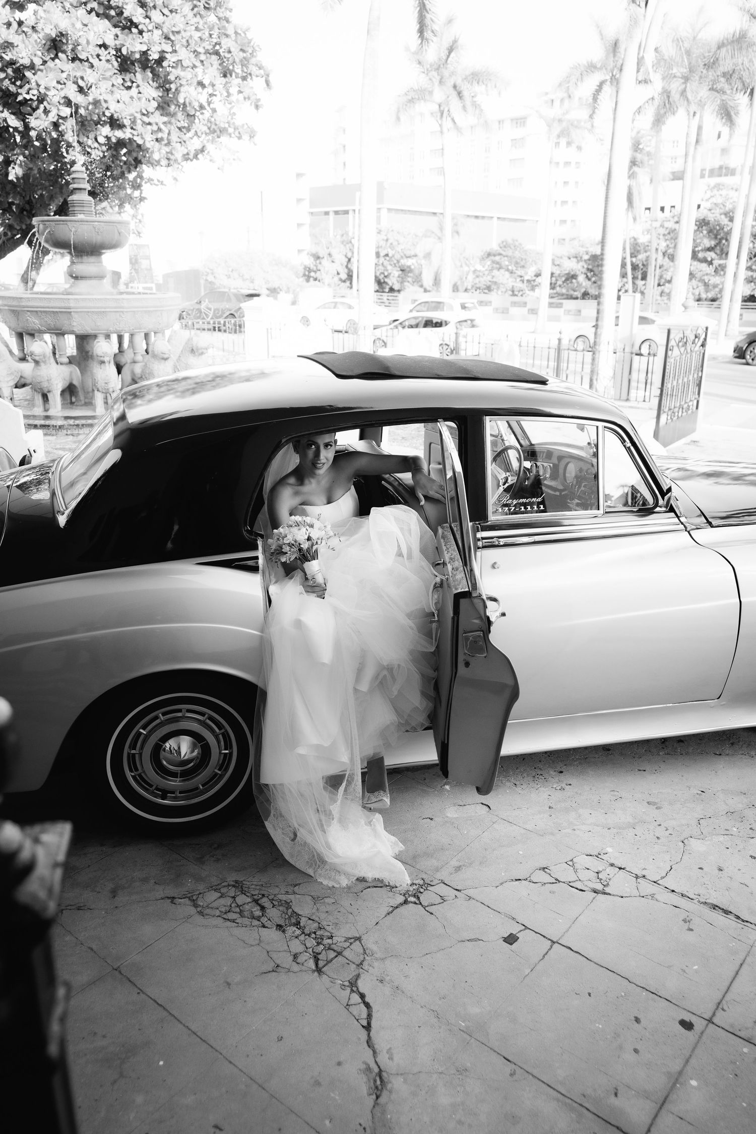 A classic white vintage car parked outside with a flowing wedding dress visible through the open door.