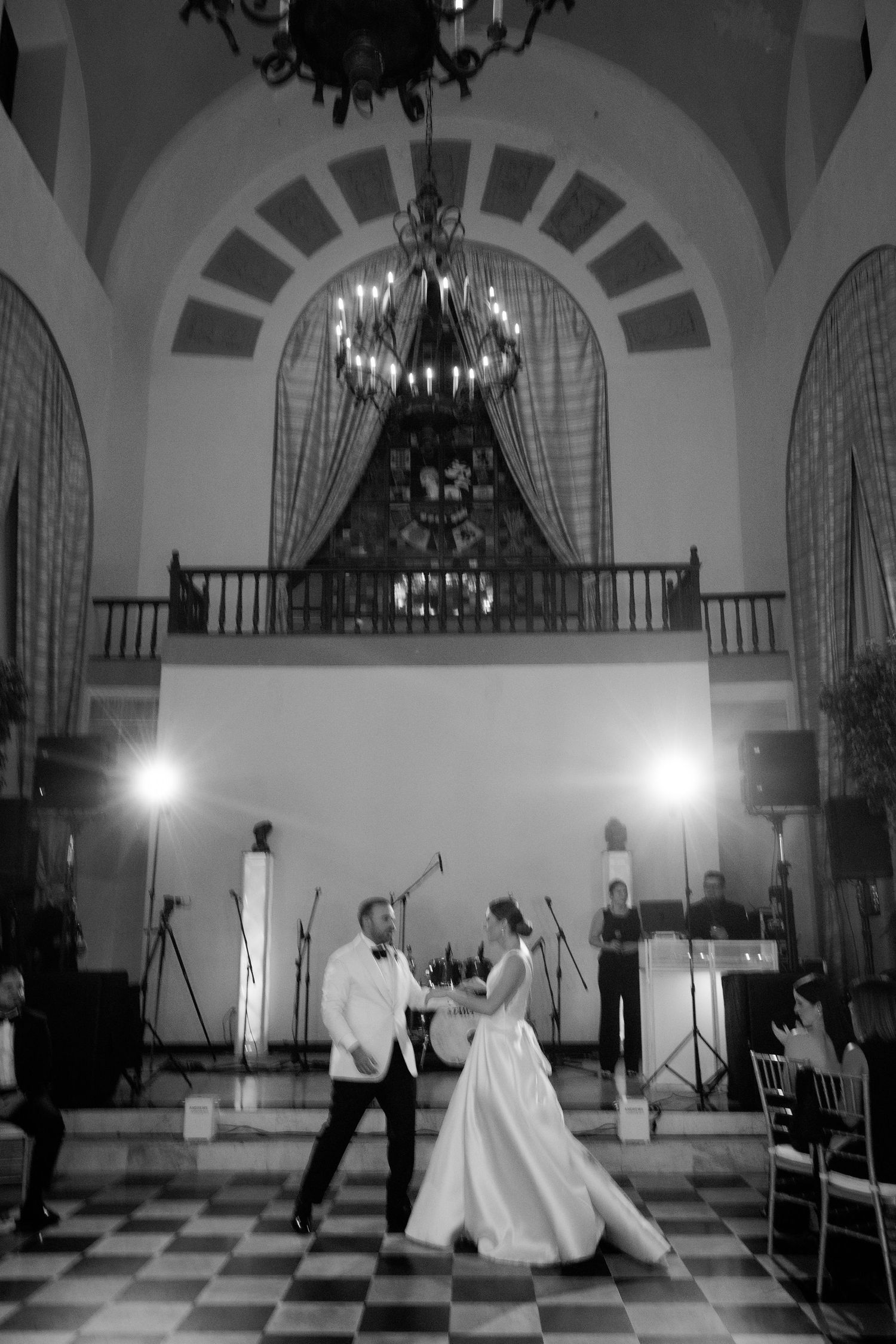 Black and white photo series showing a wedding reception dance in a grand ballroom with arched windows and chandeliers.