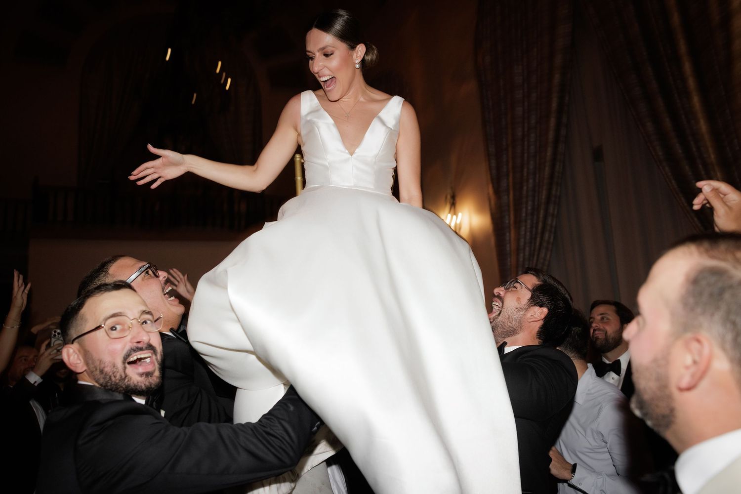 Bride and groom share a joyful dance moment with wedding guests at an elegant indoor reception.