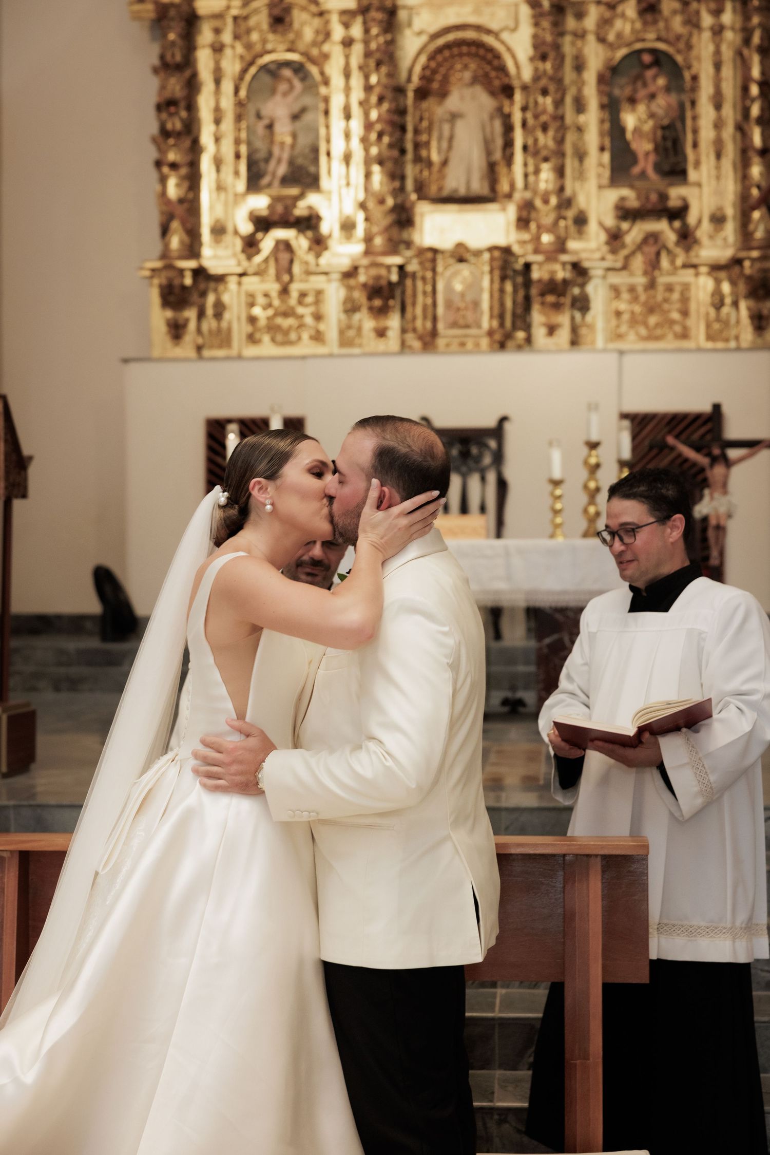 Couple shares their first kiss at the altar in an ornate church with gold decorative elements.
