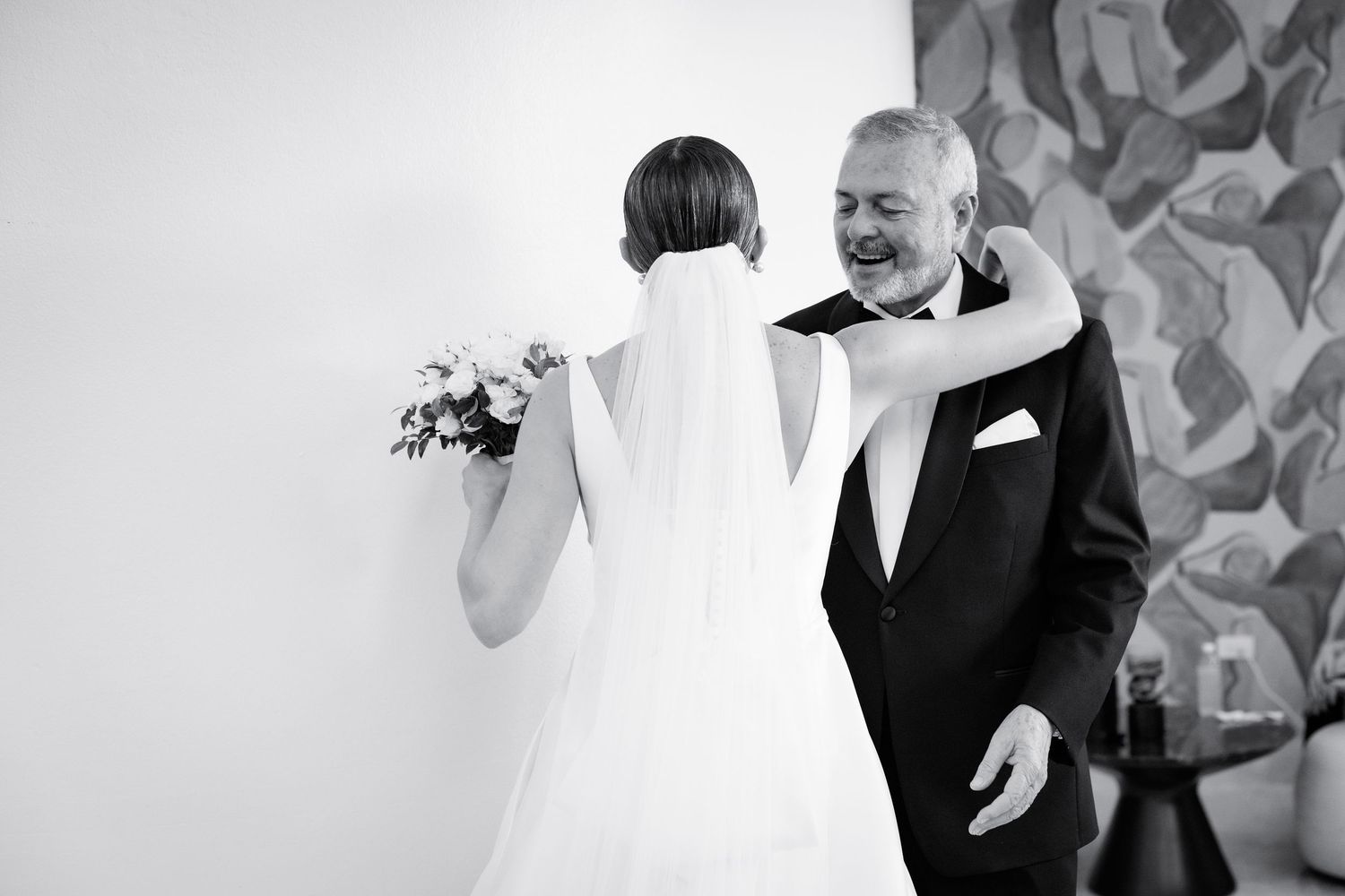 Black and white candid moment between a bride in white dress and person in formal attire.