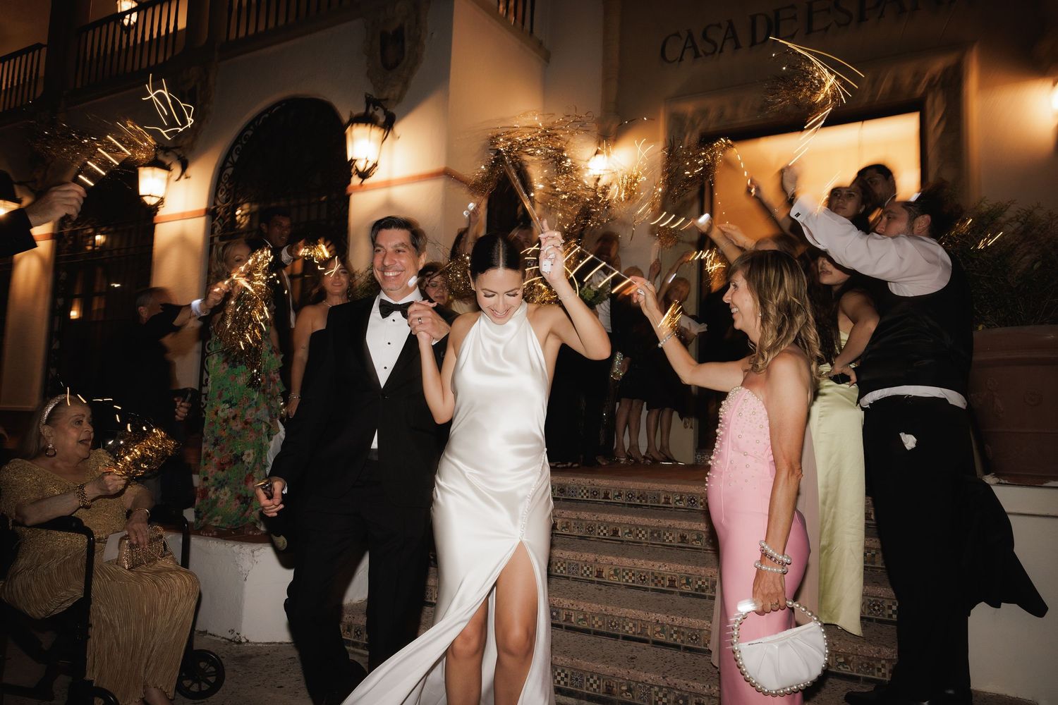 Wedding party celebrates on steps at night with sparklers creating festive atmosphere.