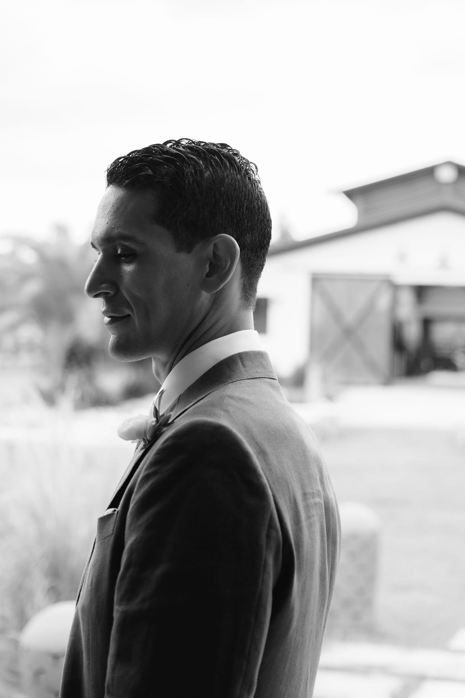 A profile portrait in black and white showing a suited figure against a rustic backdrop.
