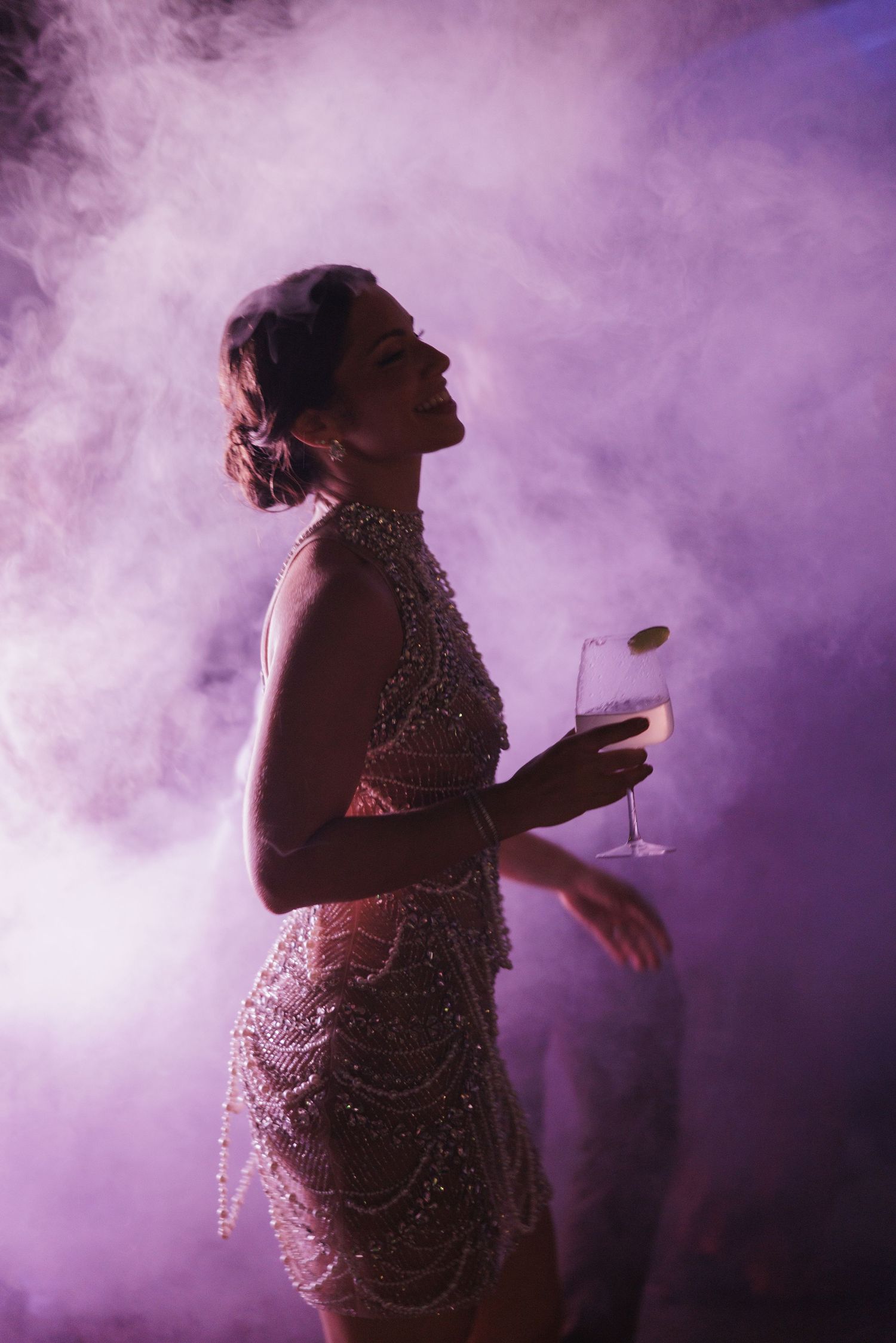 A performer in a sparkly dress dances through purple stage fog during an energetic nightclub performance.