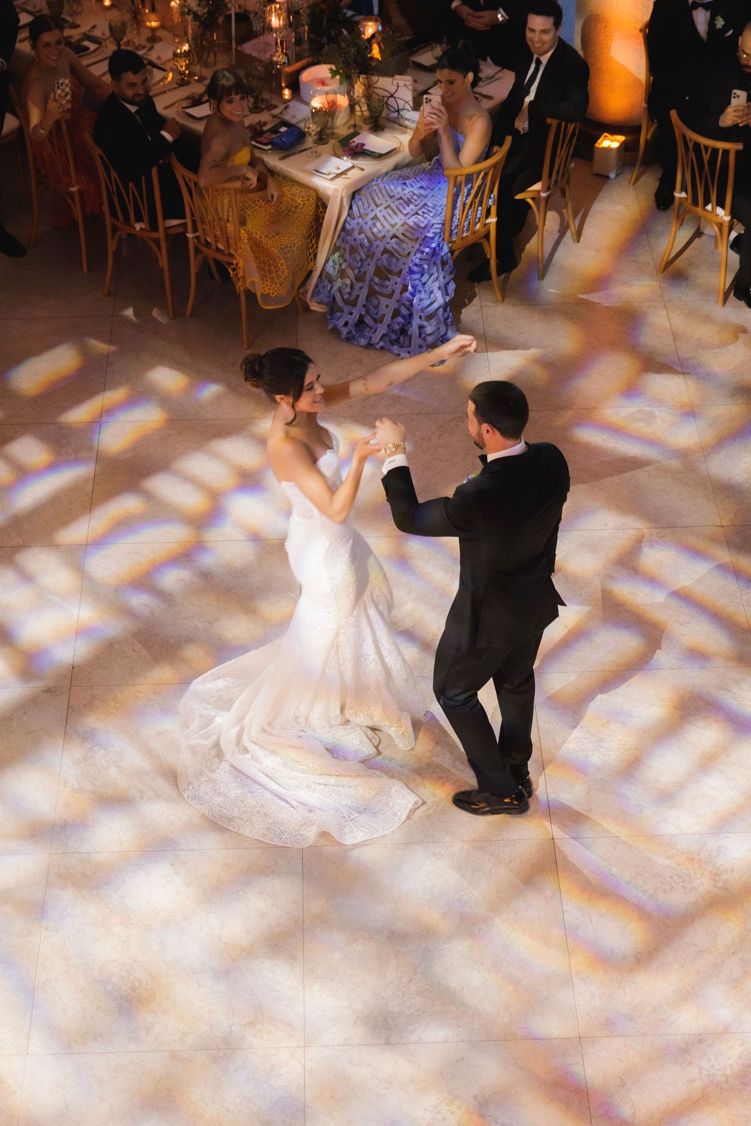 A couple performs their first dance at a wedding reception as guests watch from their tables in a beautifully lit ballroom.