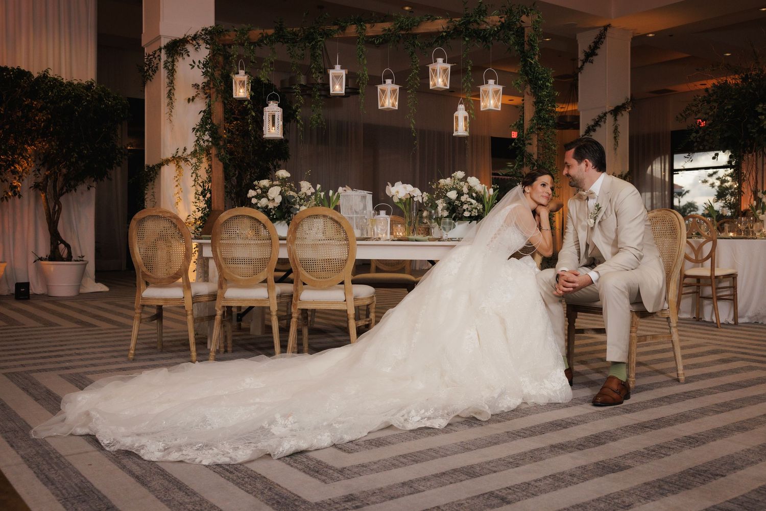 A couple shares a romantic moment at a rustic venue decorated with lanterns, barrels and soft lighting.