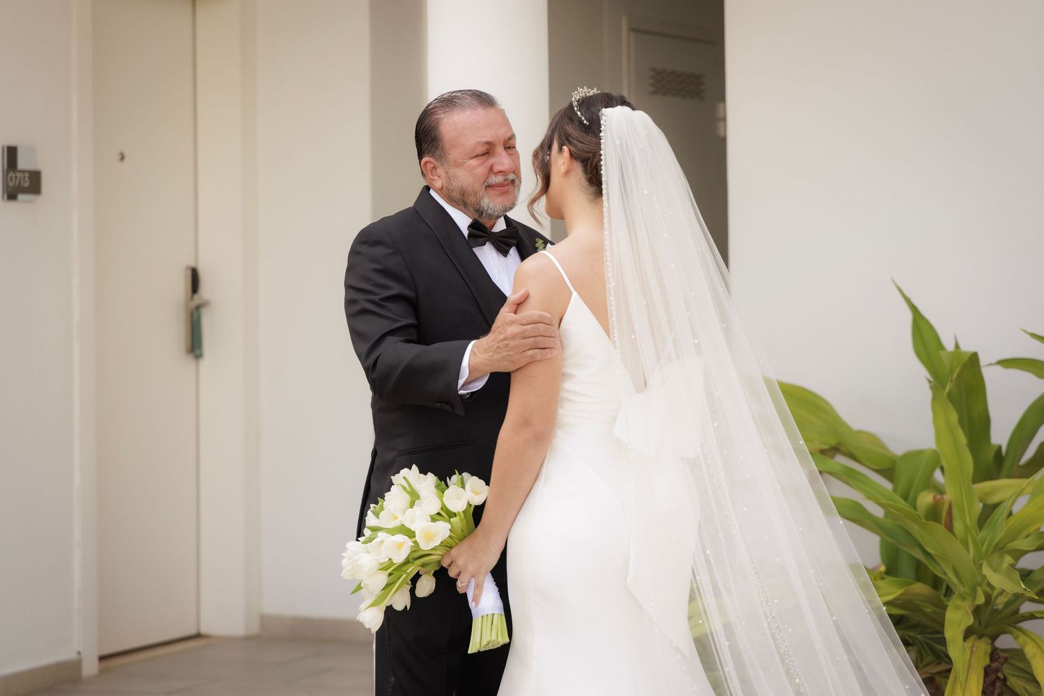 A romantic wedding moment captured as the couple embraces in an elegant indoor venue with lush green plants.