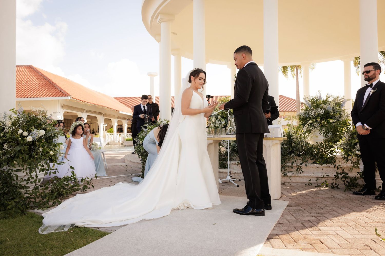 A wedding ceremony on a scenic terrace with palm trees and coastal sunset lighting creates a romantic ambiance.
