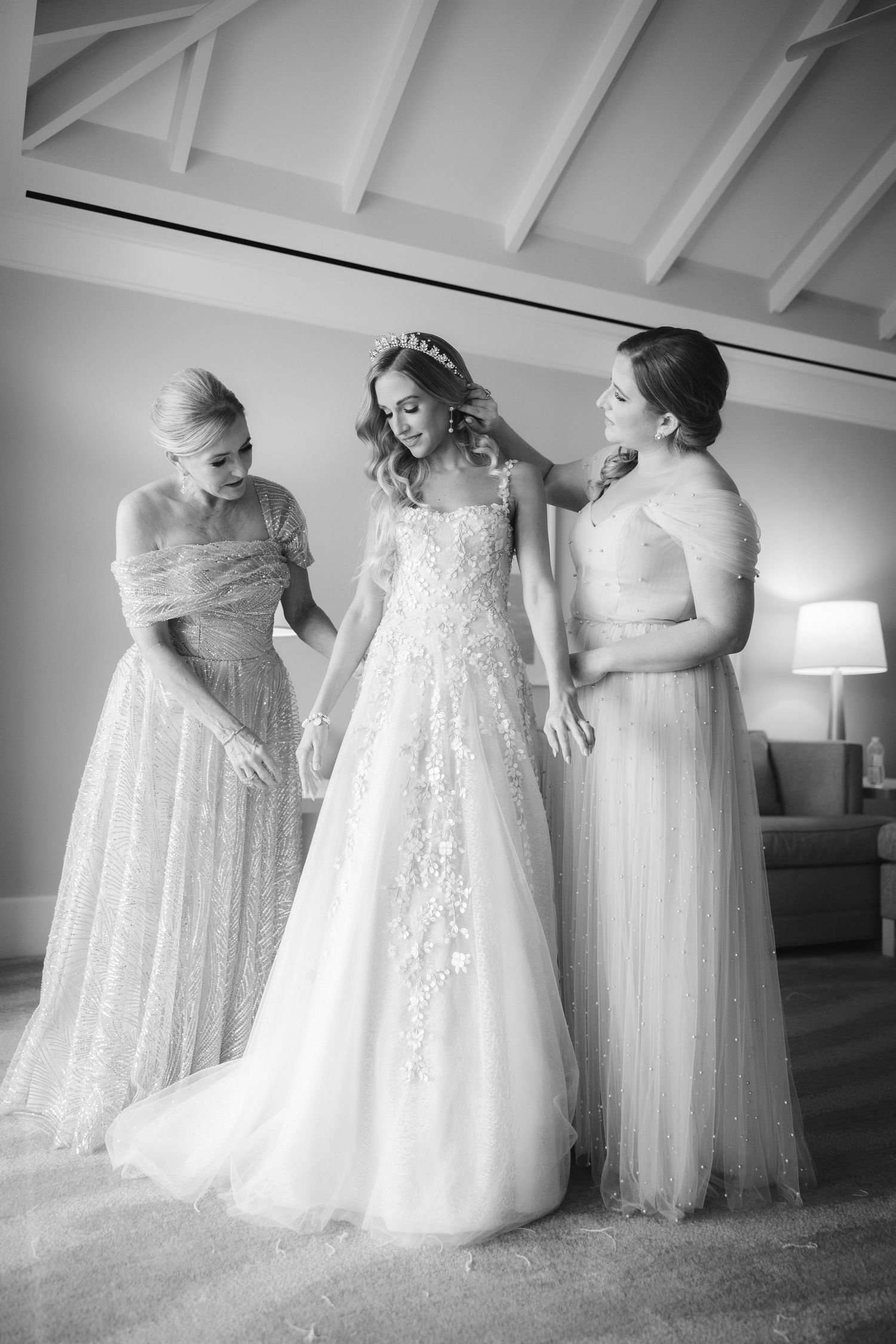 Black and white photo showing three formal dresses in white or light colors standing together in an elegant display.