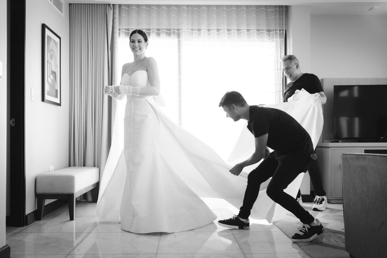A series of black and white wedding preparation photographs showing dress adjustments and fittings in an elegant room.