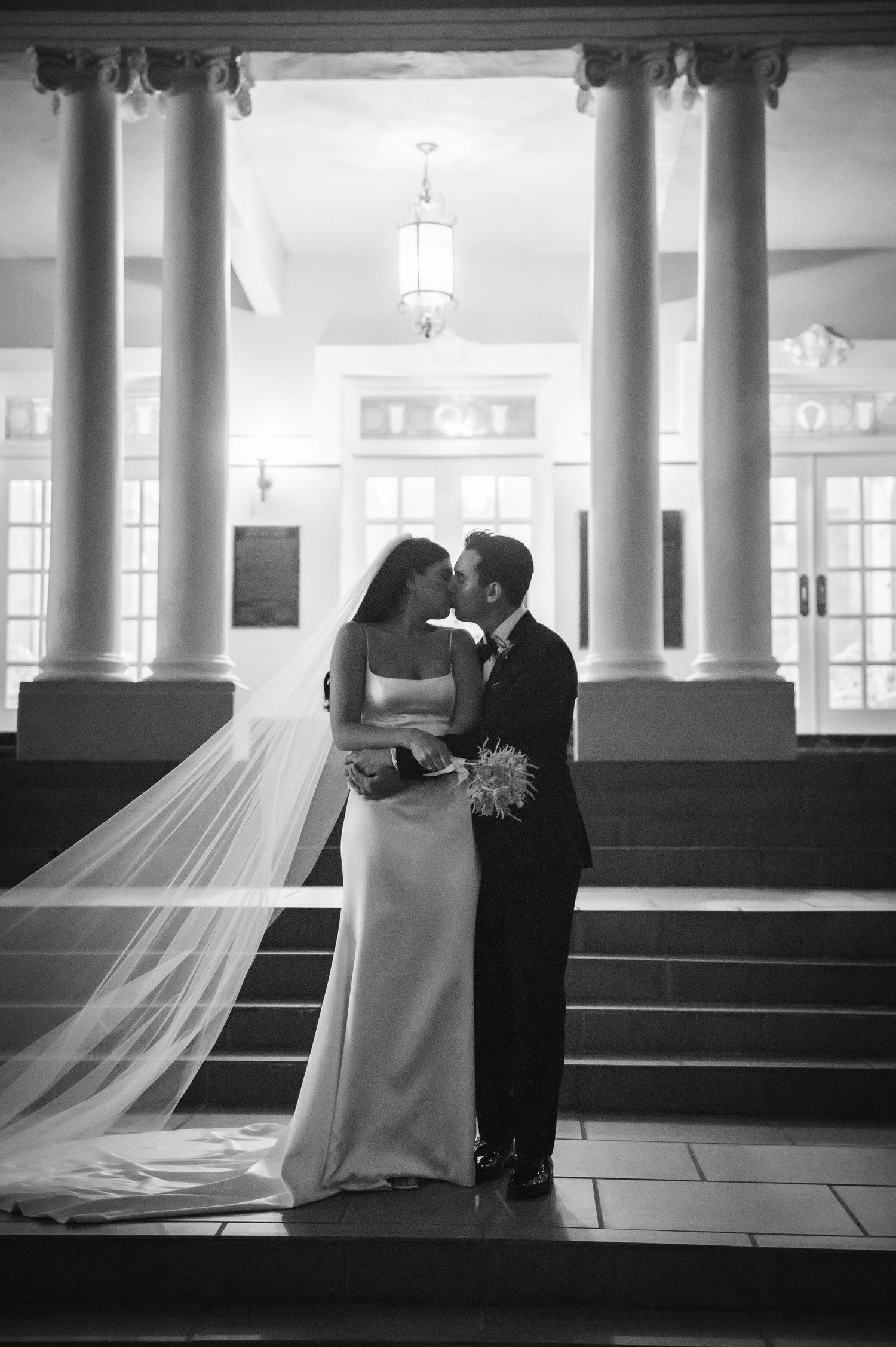 Black and white wedding photo series showing couple among classical white pillars in historic interior.