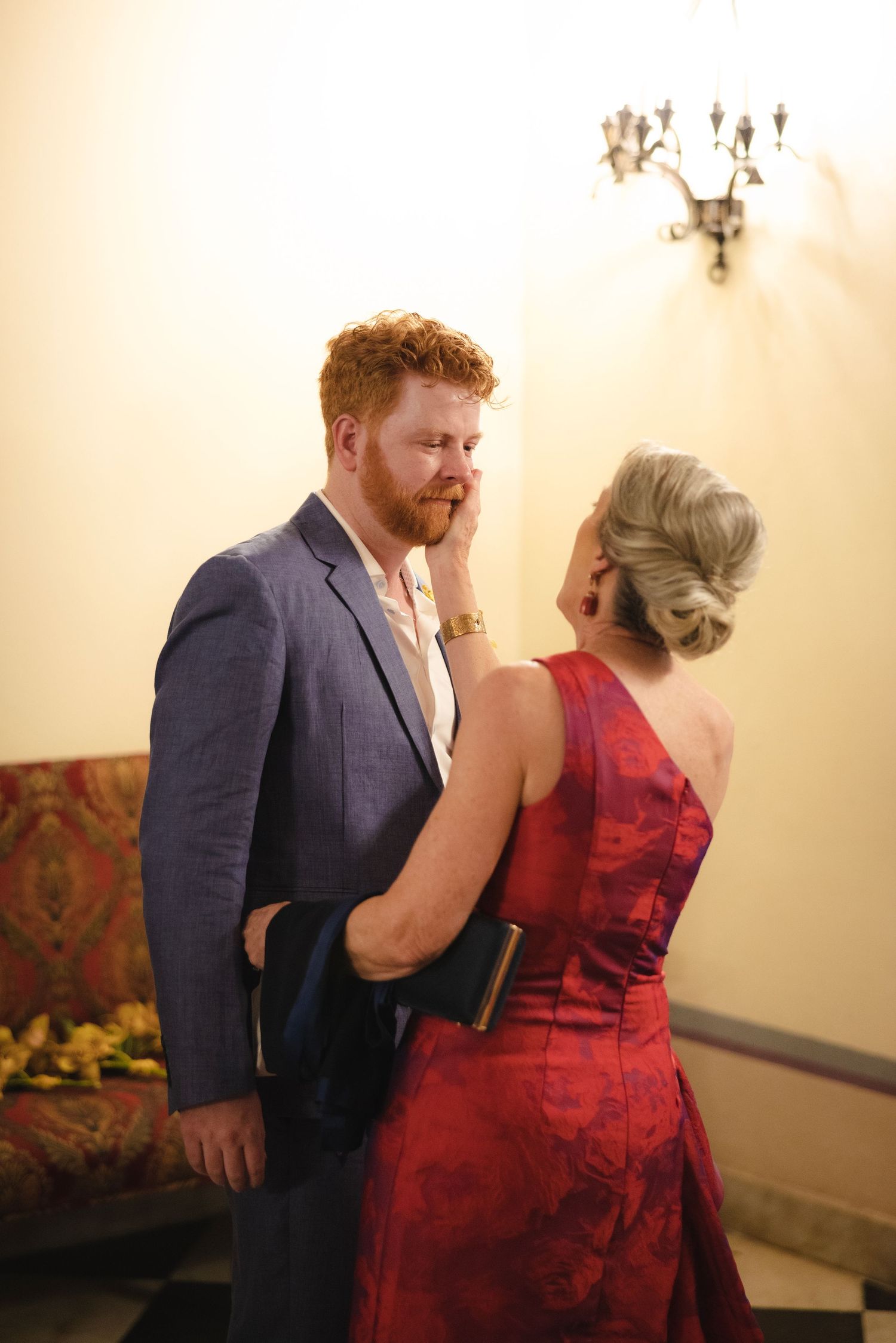 A couple shares an intimate moment in formal attire, with the woman wearing a striking red dress and man in a navy suit.