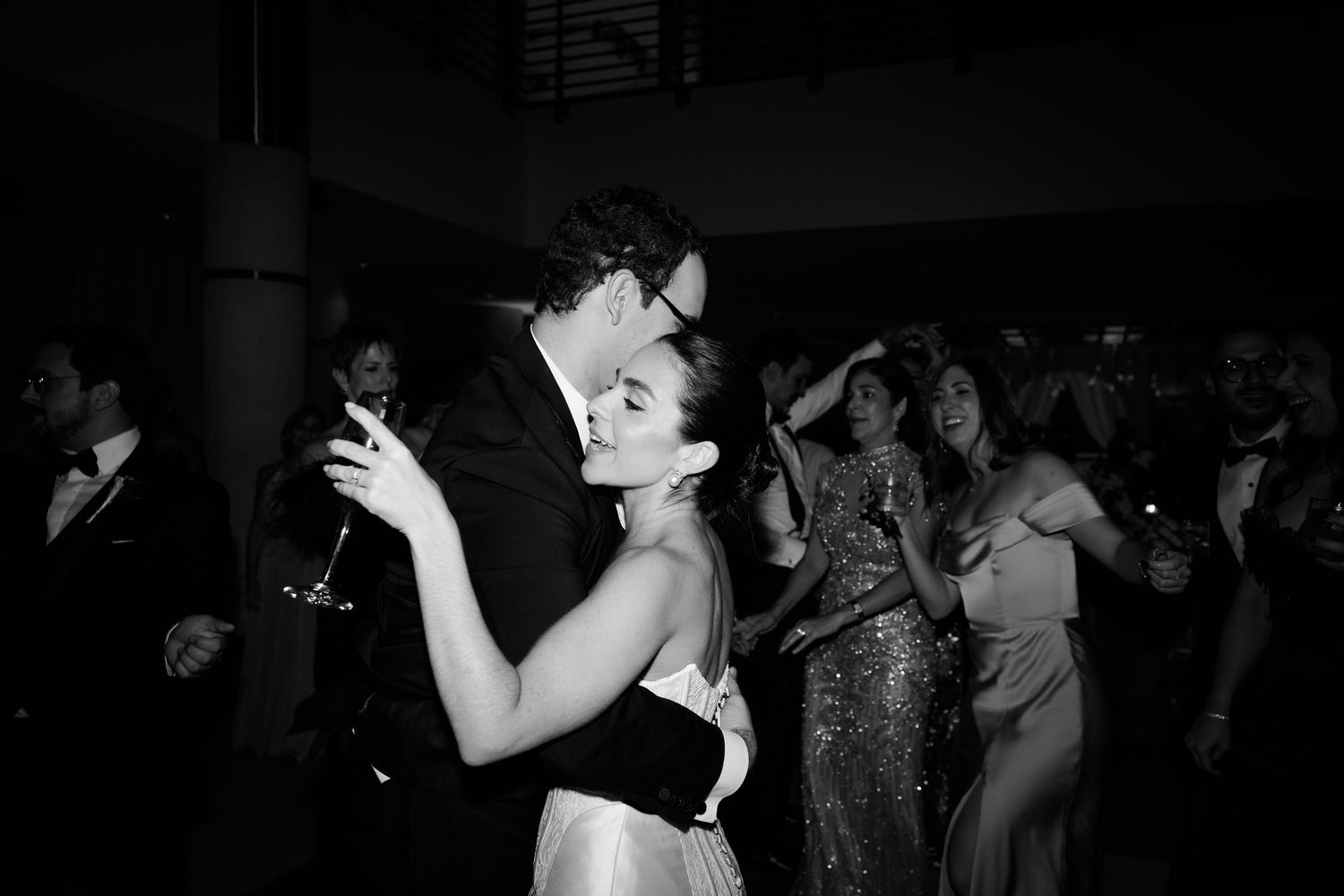 A couple shares an intimate dance together at a dimly lit reception surrounded by other guests.