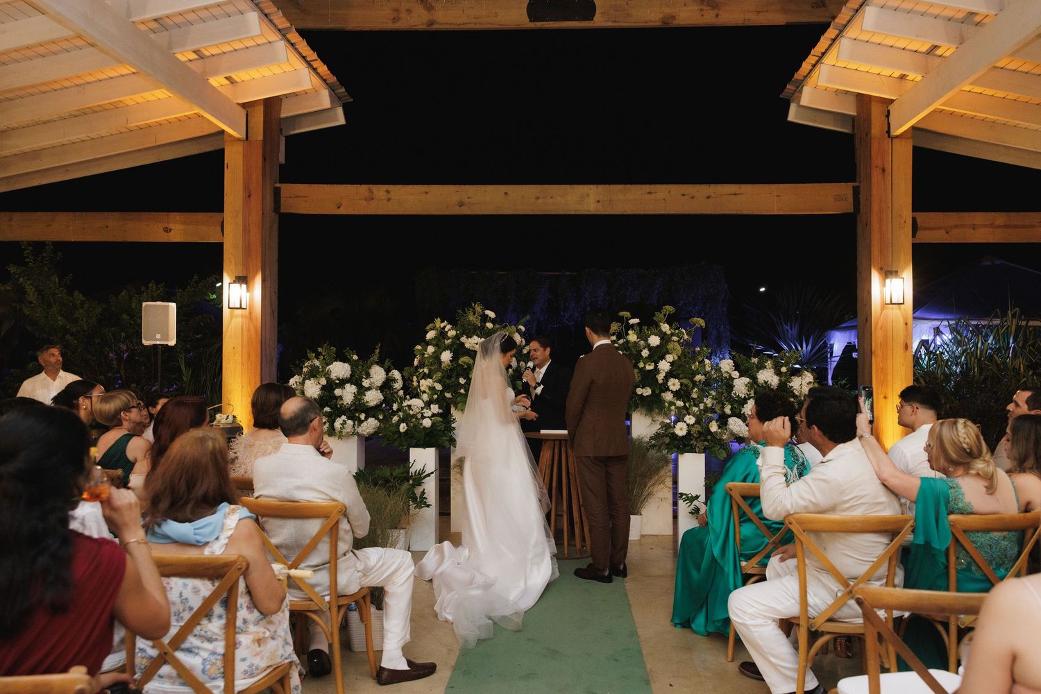 Evening wedding celebration with guests dancing under wooden beams and string lights.