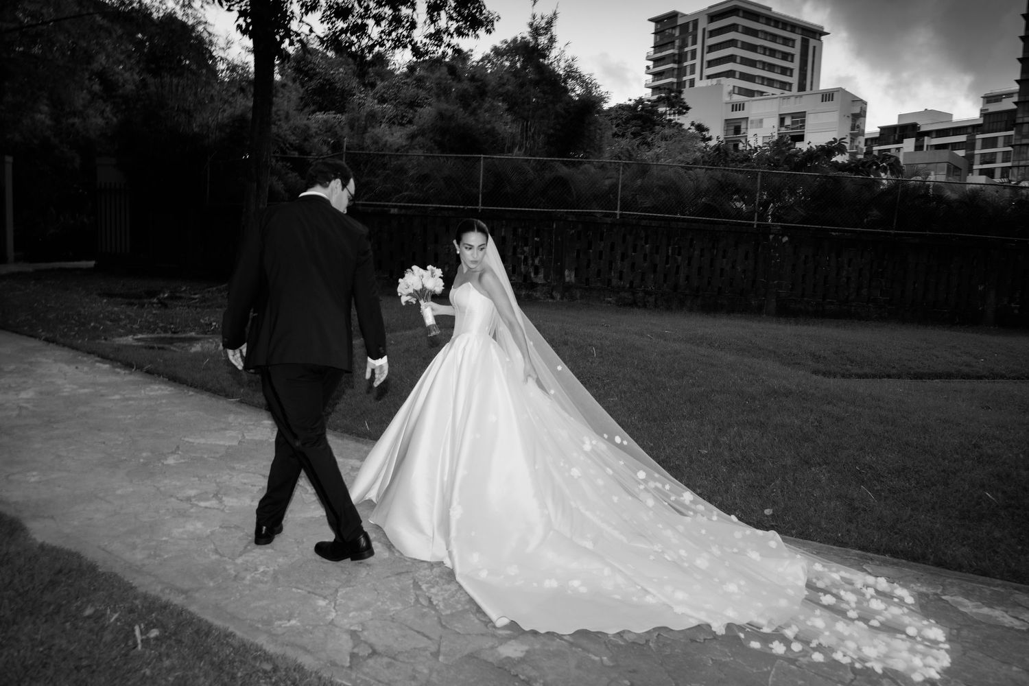 A black and white wedding photography sequence shows a couple walking together in an outdoor garden setting.