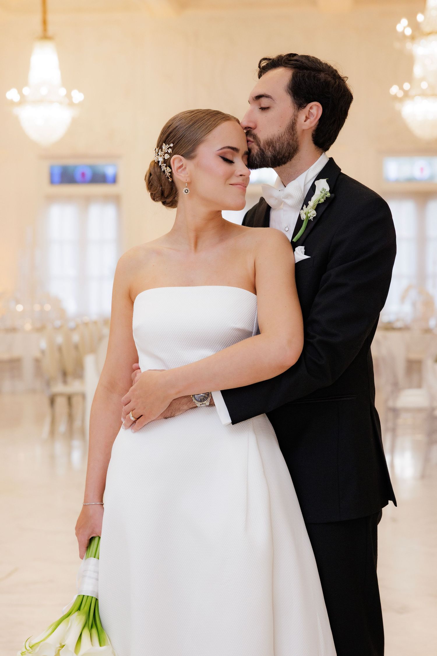 An intimate wedding moment shared in an elegant ballroom with crystal chandeliers and white decor.