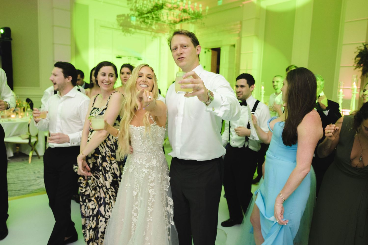 Wedding guests dancing and socializing in a ballroom bathed in green ambient lighting.