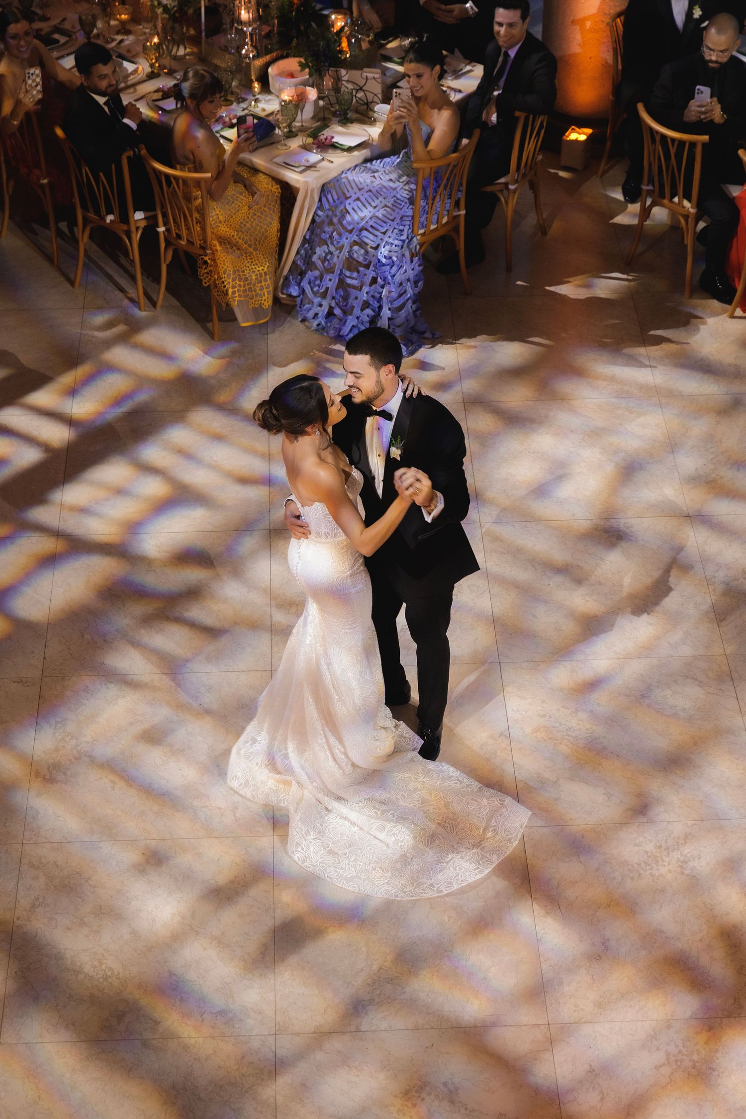 A romantic first dance between newlyweds on an elegant dance floor with dramatic lighting creating a magical atmosphere.