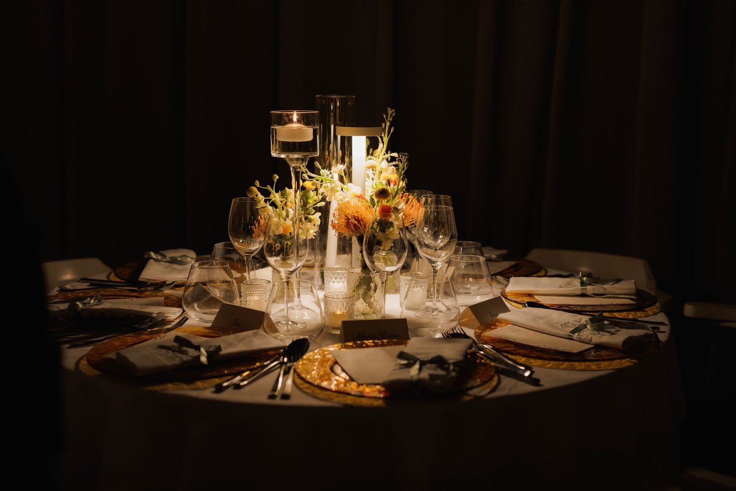 Elegant formal table setting with candles and floral centerpiece glowing in warm light at night.