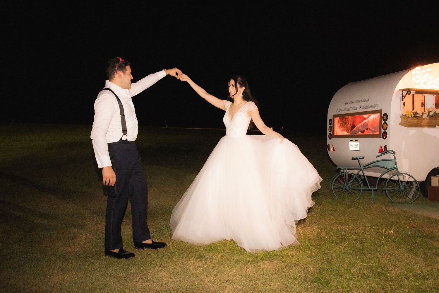 A couple dances together at an outdoor evening wedding reception, with the bride wearing a white tulle gown.