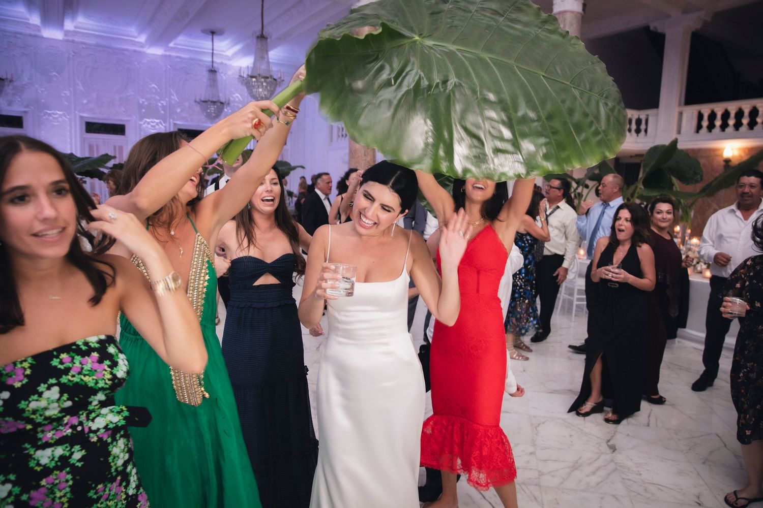 Wedding celebration with guests dancing and mingling in formal attire under decorative venue lighting.