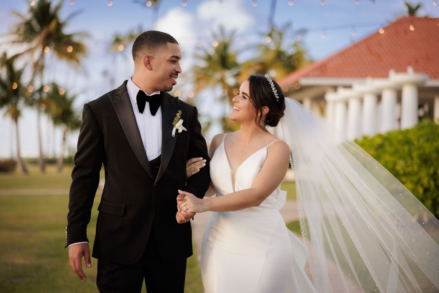 Happy wedding couple shares tender moment in scenic outdoor tropical setting with palm trees at sunset.