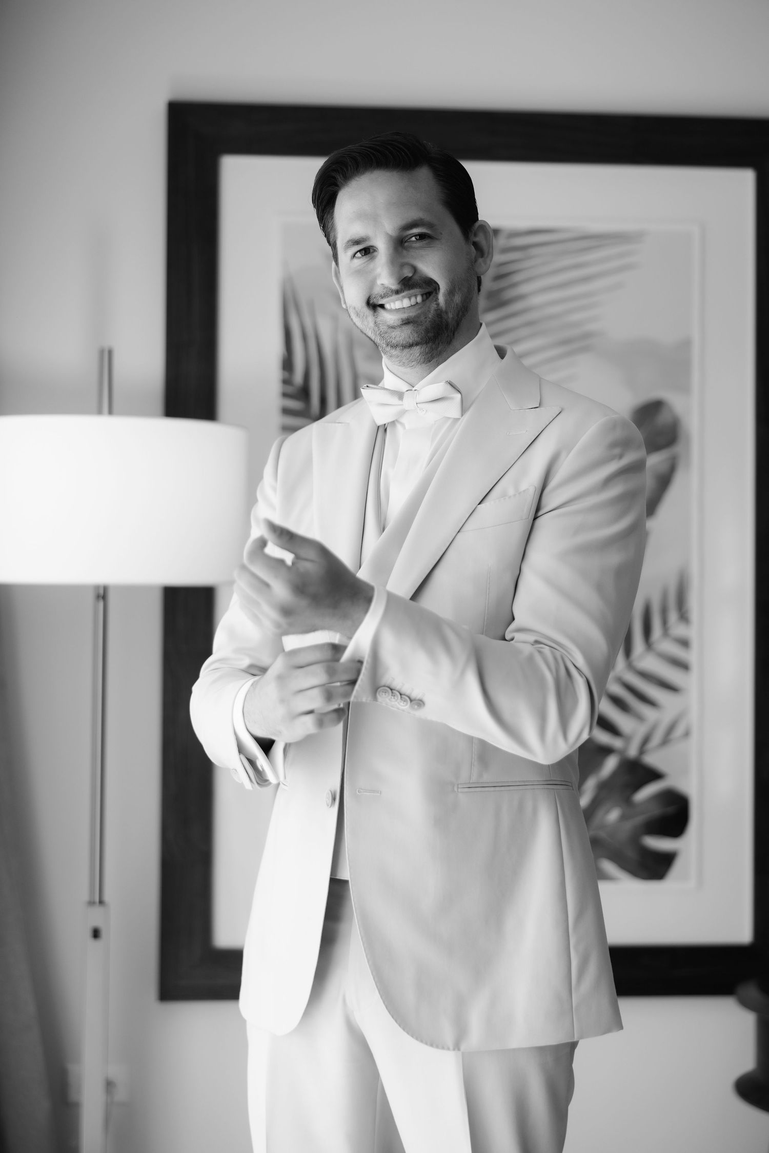 A gentleman in a white suit adjusts his tie while getting ready in black and white photography.