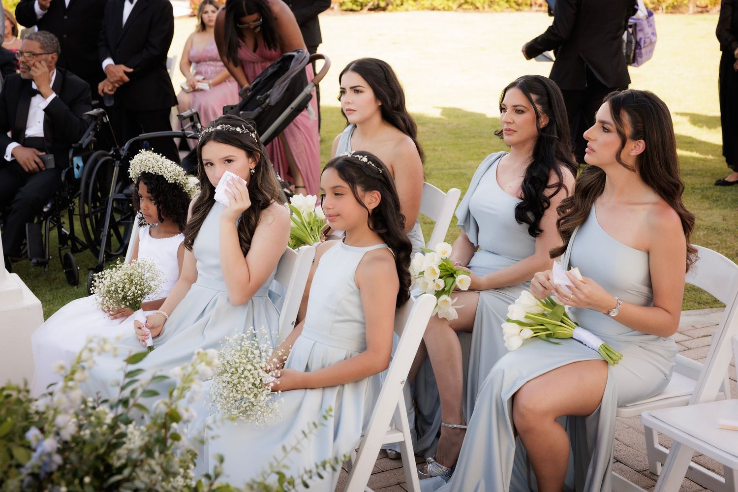 Wedding party attendees in light colored dresses gather outdoors for a candid moment during celebrations.