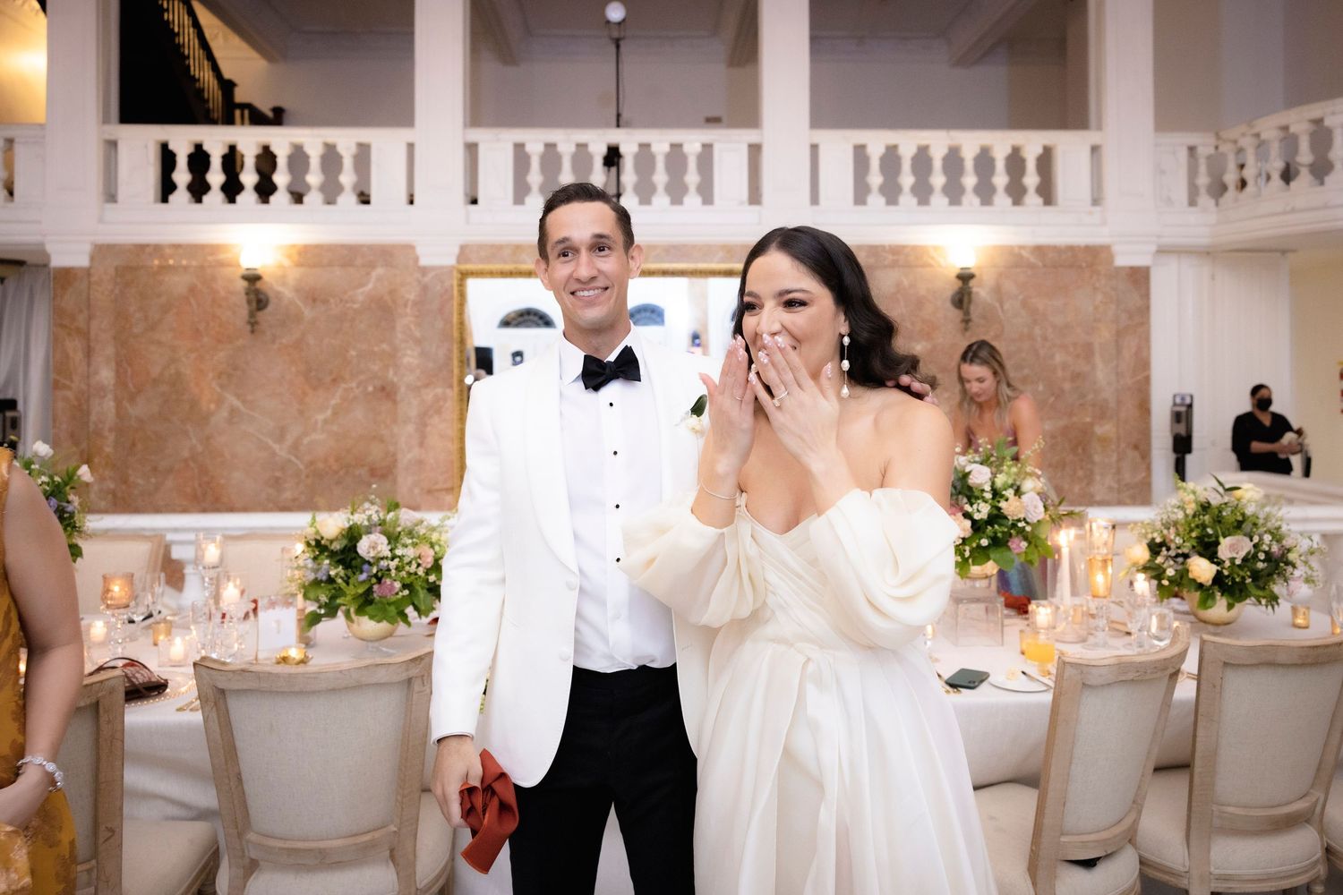 Wedding reception in a grand white ballroom with ornate columns and romantic lighting.