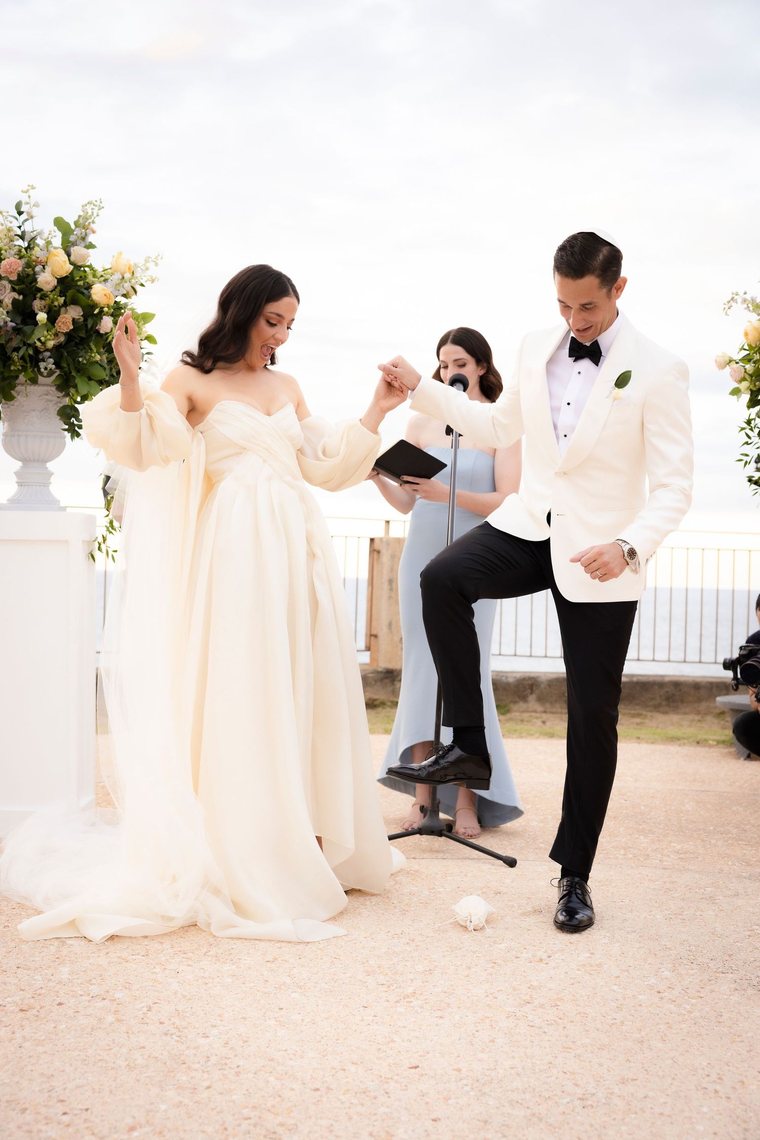 Wedding party celebrates on an outdoor terrace with decorative white pillars and floral arrangements.
