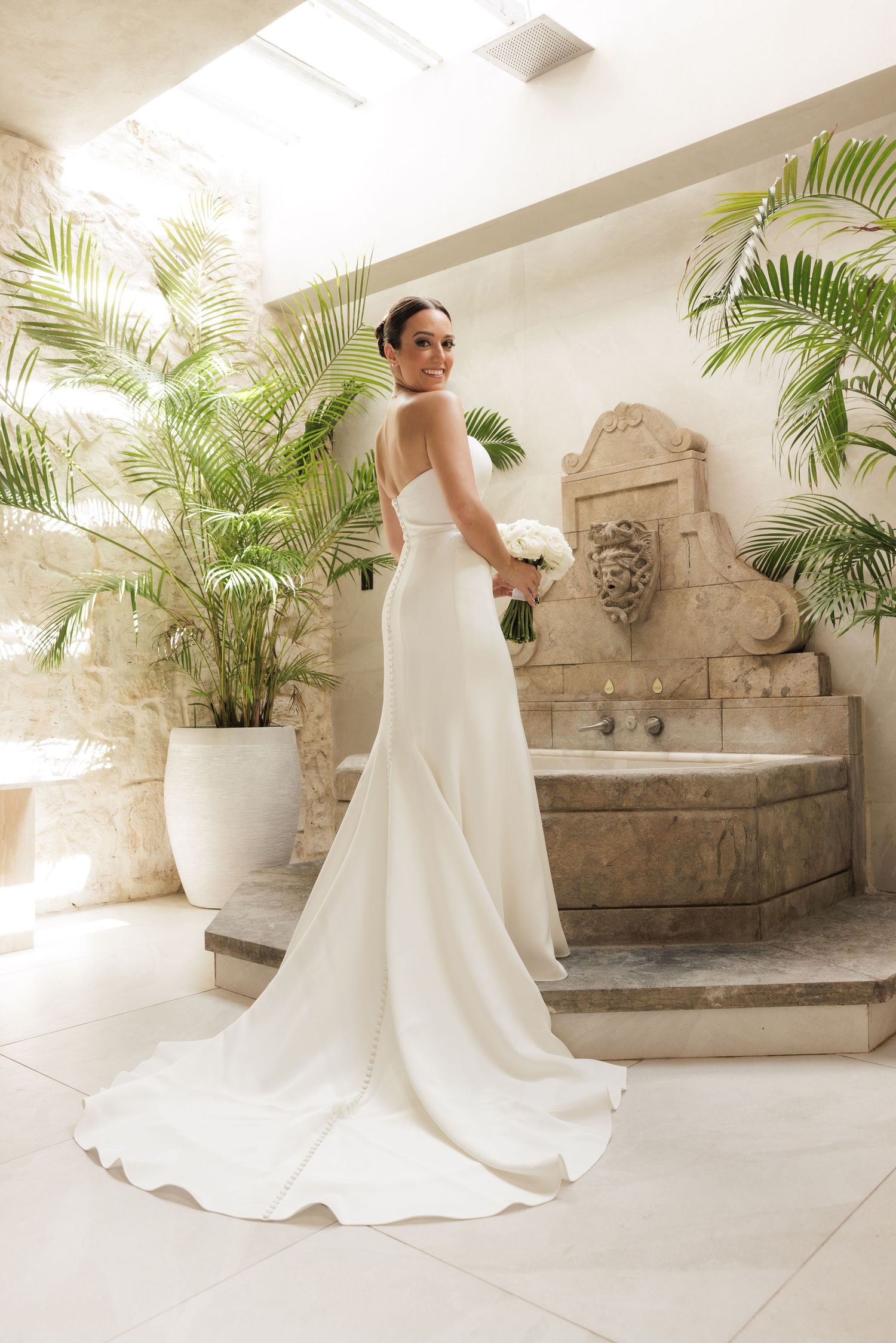 Wedding dress photographed against stone fountain backdrop with tropical greenery.