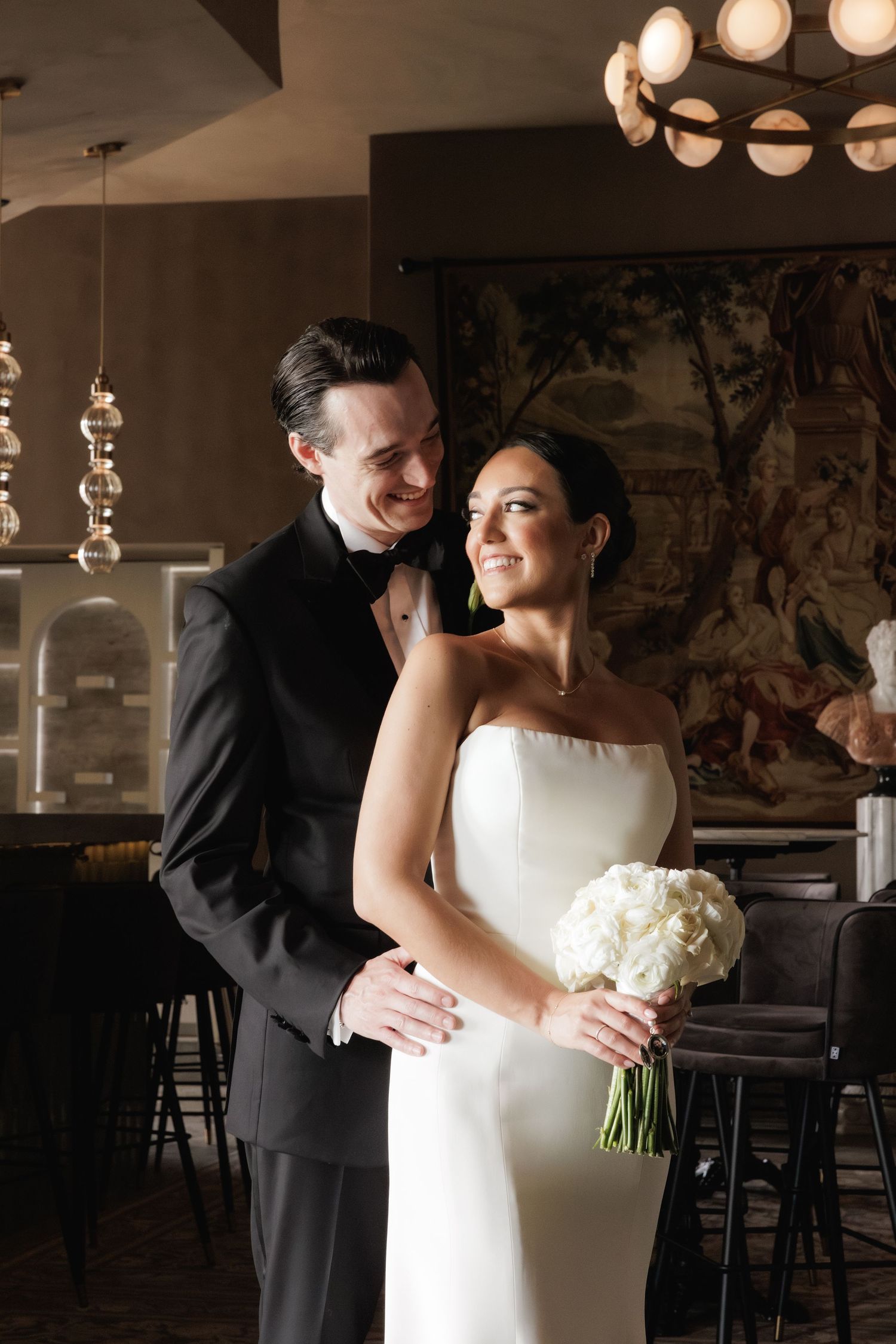 Romantic moment between newlyweds dancing in dimly lit venue with modern pendant lights overhead.