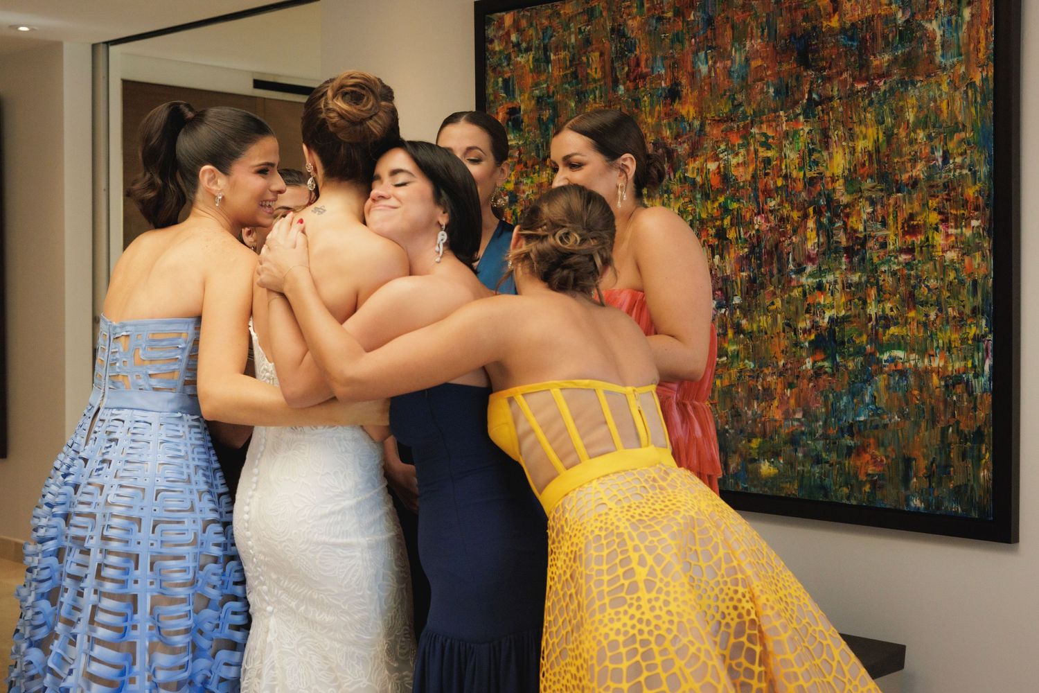 Wedding party gathered in front of vibrant abstract painting wearing blue and yellow dresses.