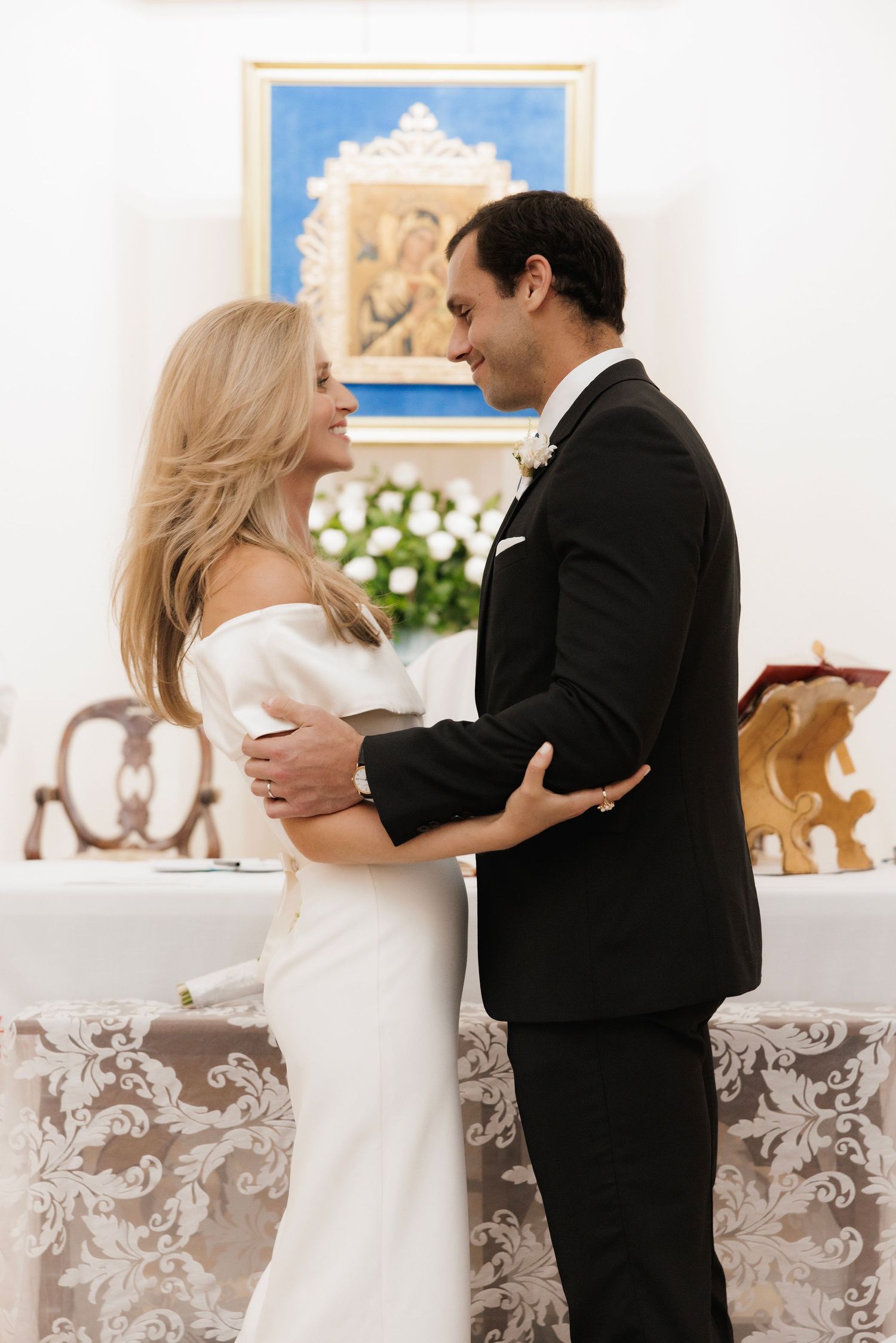 A couple in formal attire share an intimate dance, with the bride in white and groom in black against an elegant backdrop.