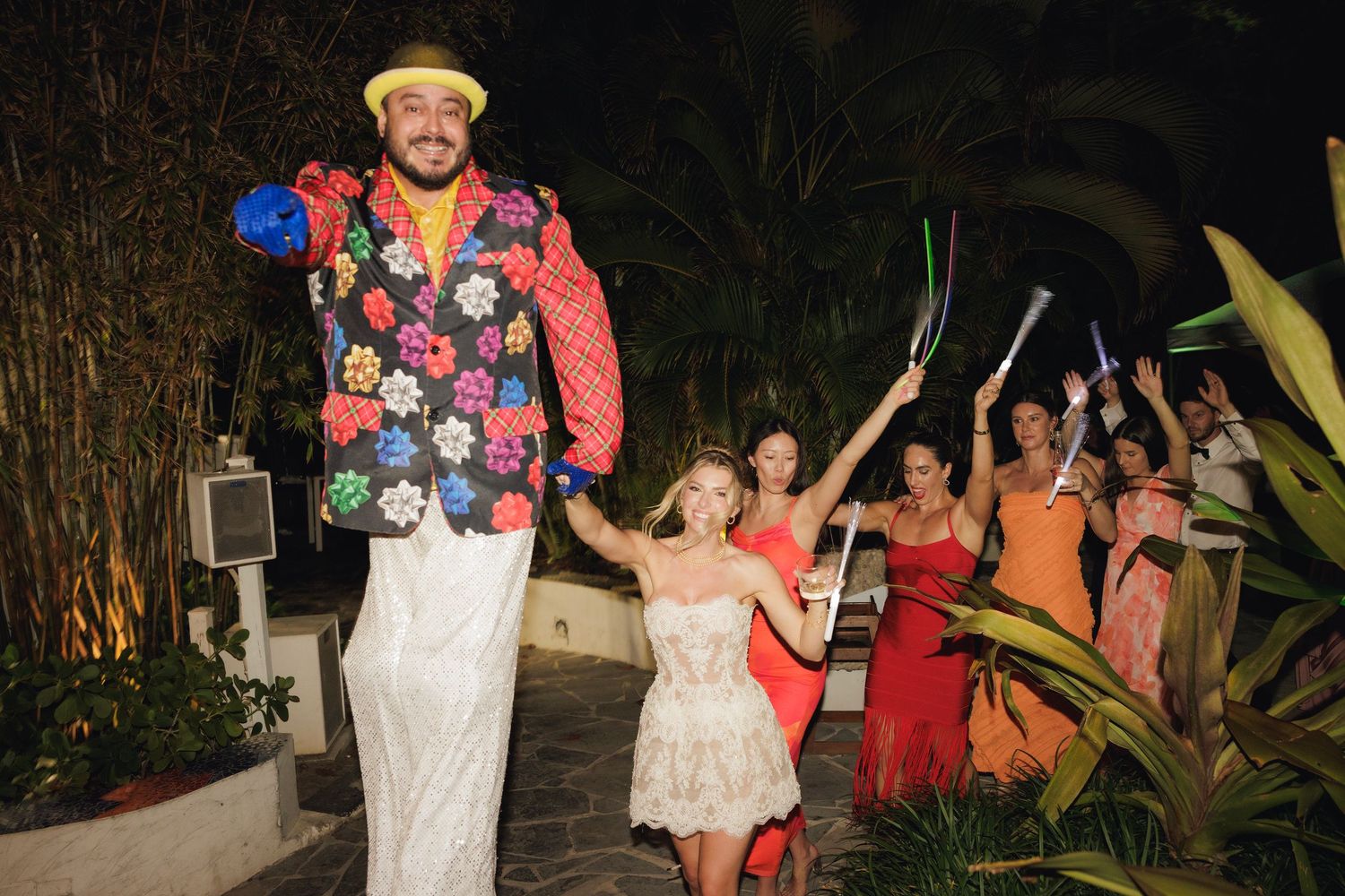 People celebrating outdoors at night with festive outfits and colorful decorations in a garden setting.