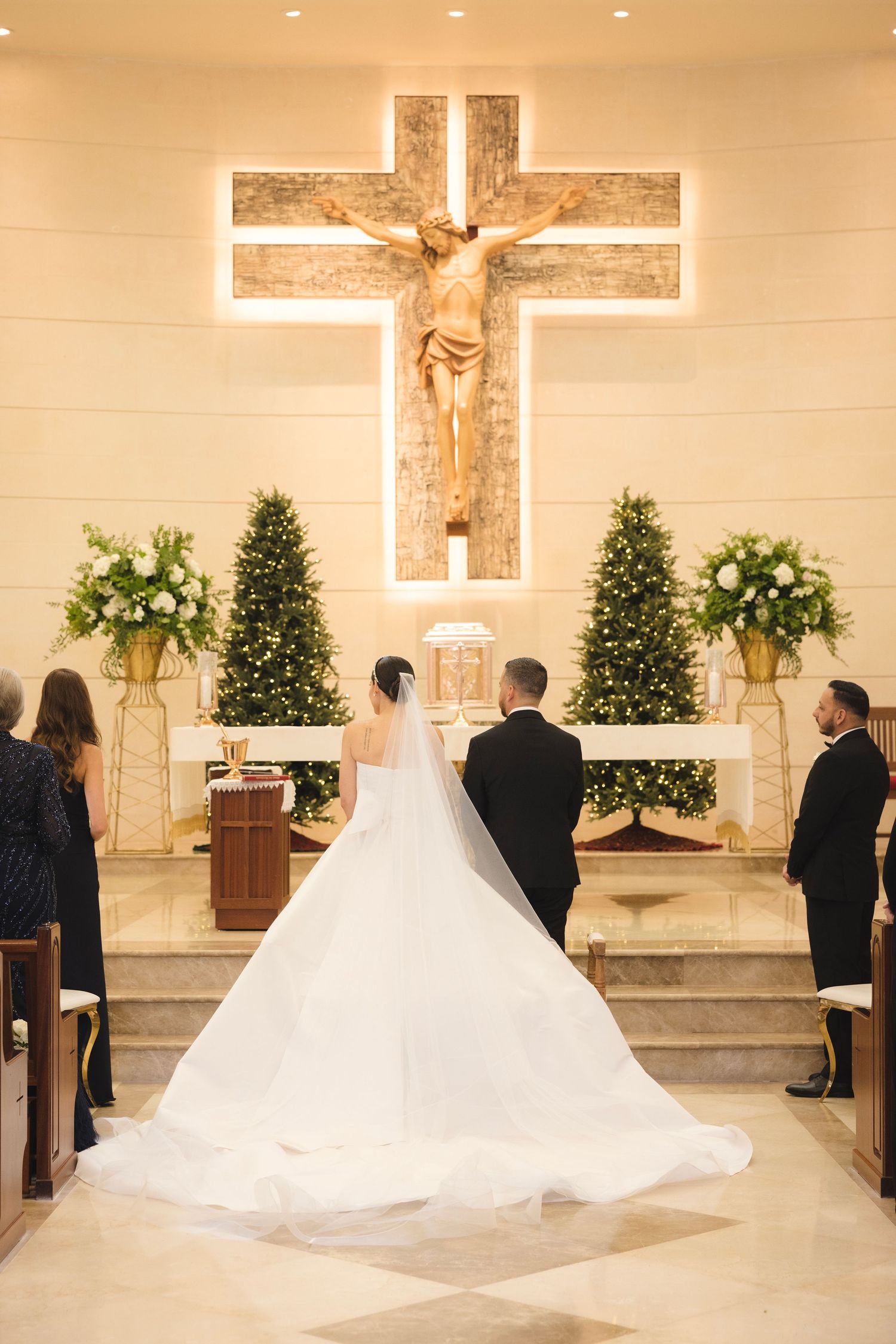 Elegant church wedding ceremony with flowing white gown and decorative crosses on altar amid soft lighting and greenery.
