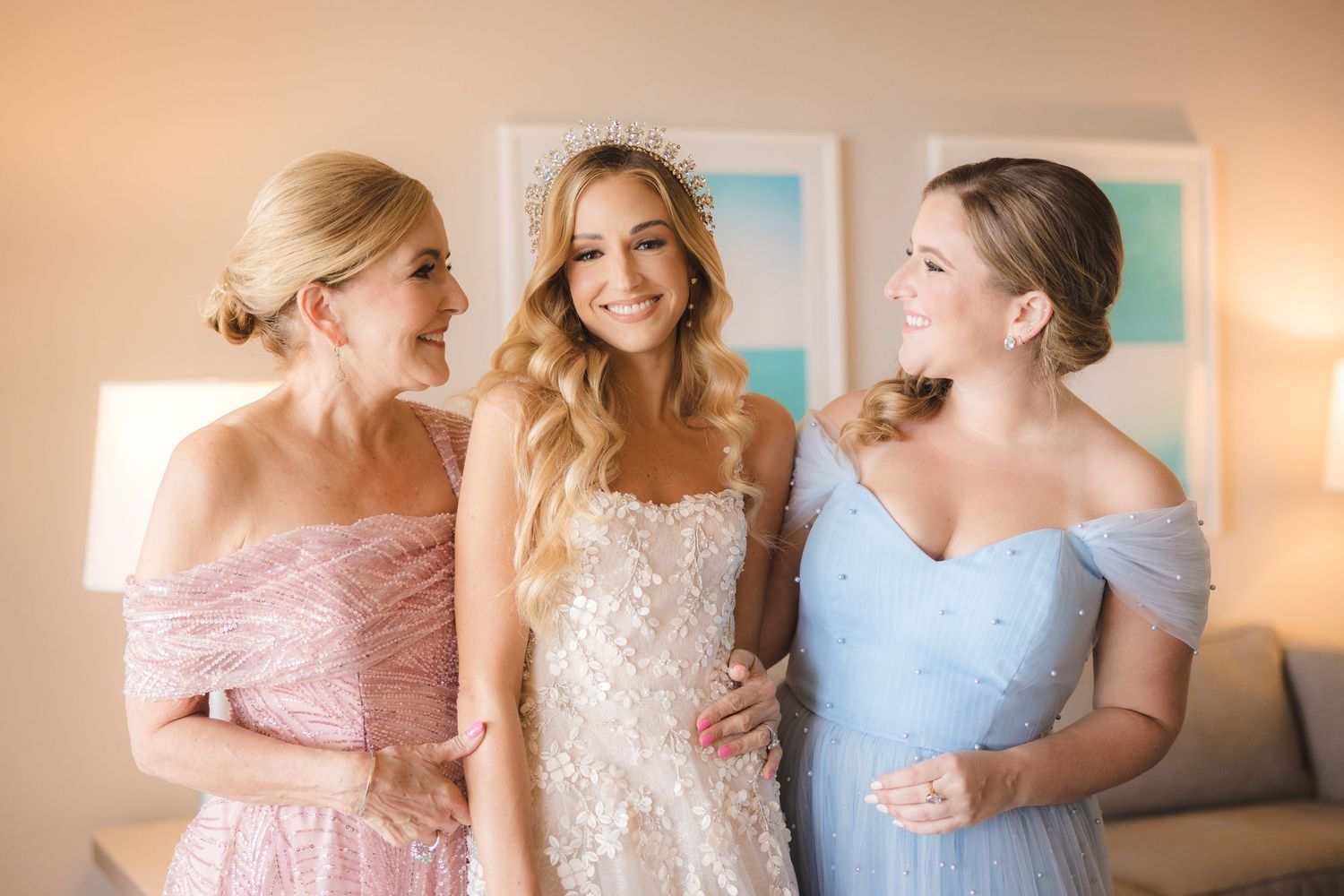 Wedding party in soft pastel pink and blue dresses celebrates joyfully in sunlit room.