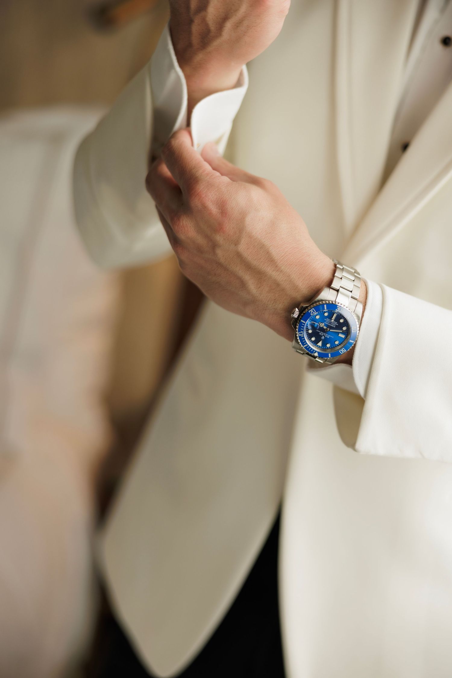Close-up of hands adjusting white suit sleeve with elegant blue-faced watch on wrist.