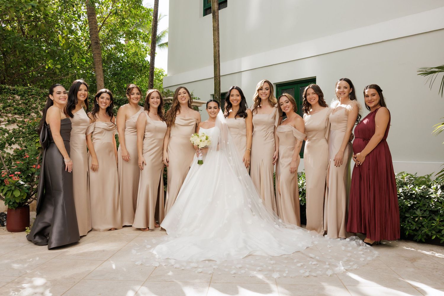 Bridesmaids in elegant champagne-colored gowns stand together outdoors for a formal wedding photo.