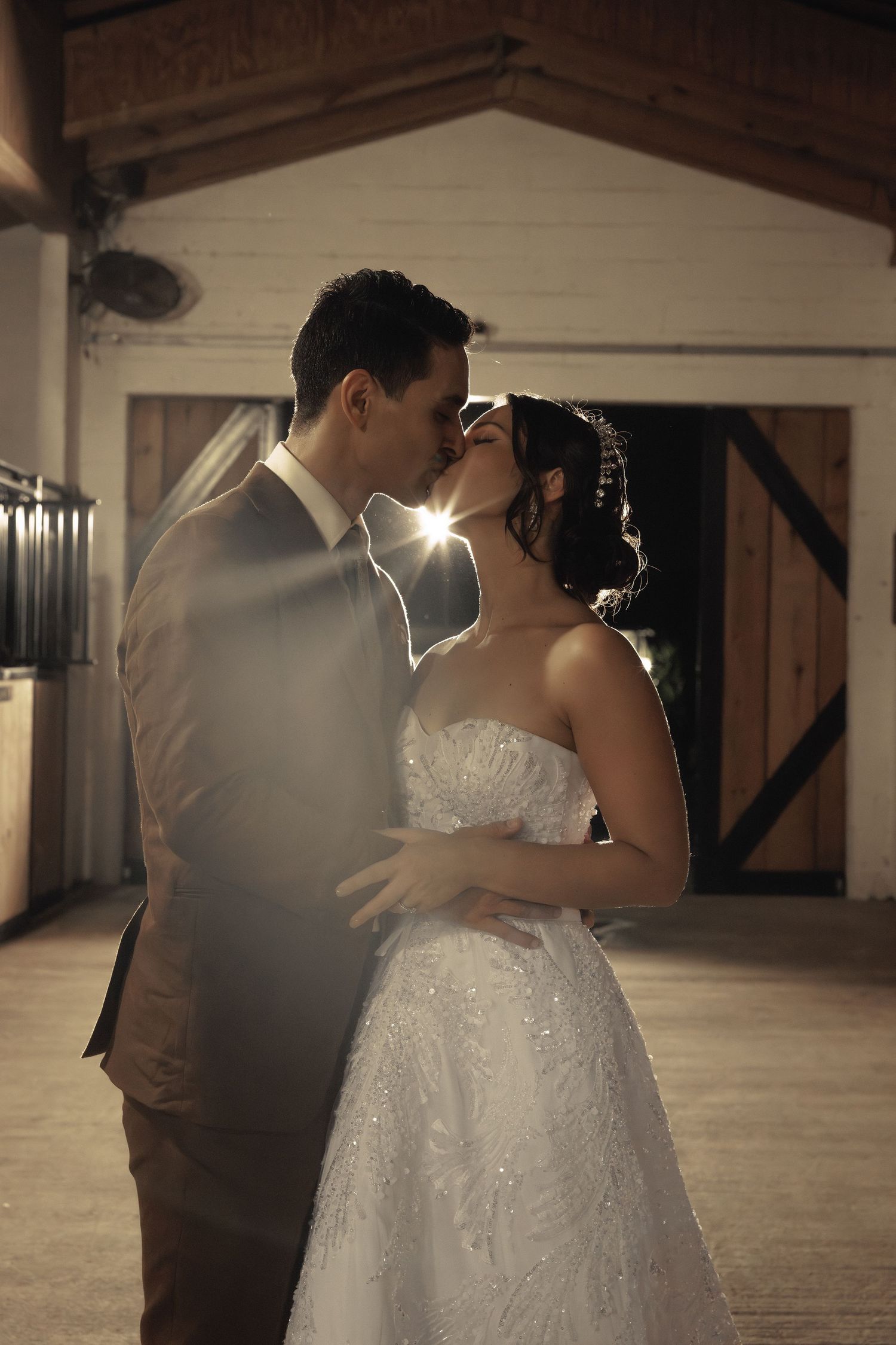 A backlit wedding couple sharing an intimate kiss with a beautiful sunburst effect in the background.