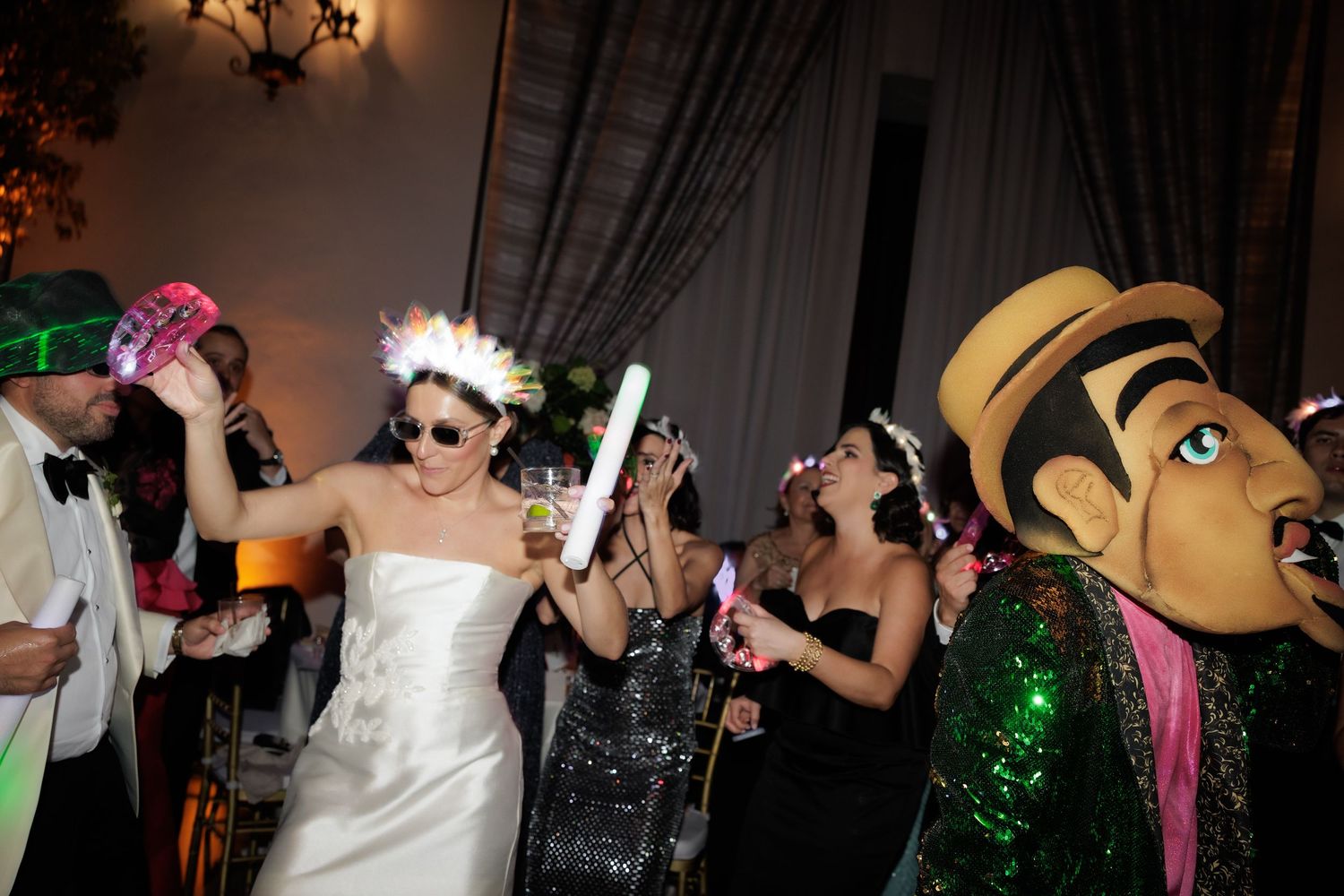 Wedding guests dance and celebrate during a lively reception with colorful lighting and decorations.