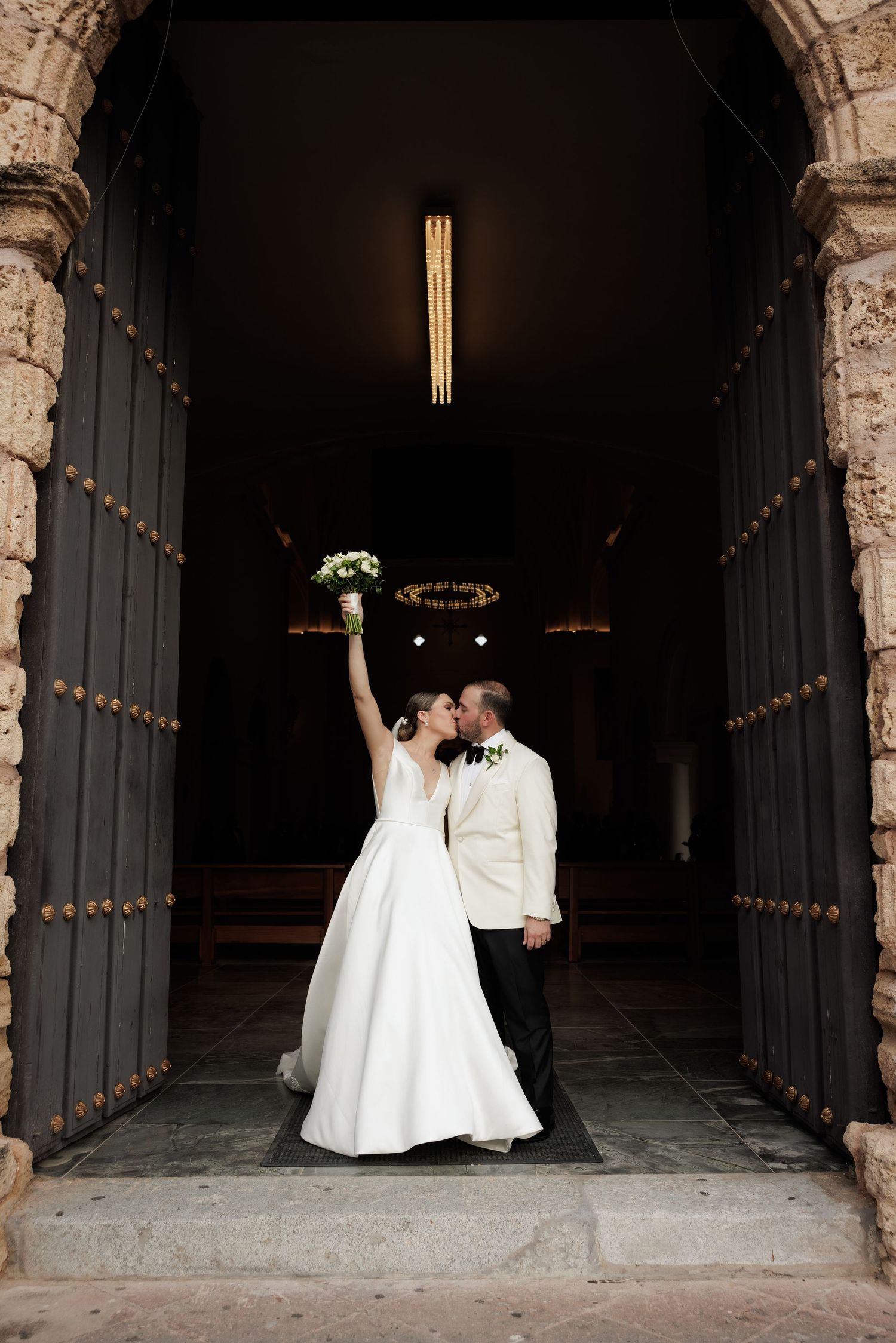 A romantic wedding moment captured in a stone archway with string lights creating a magical atmosphere.