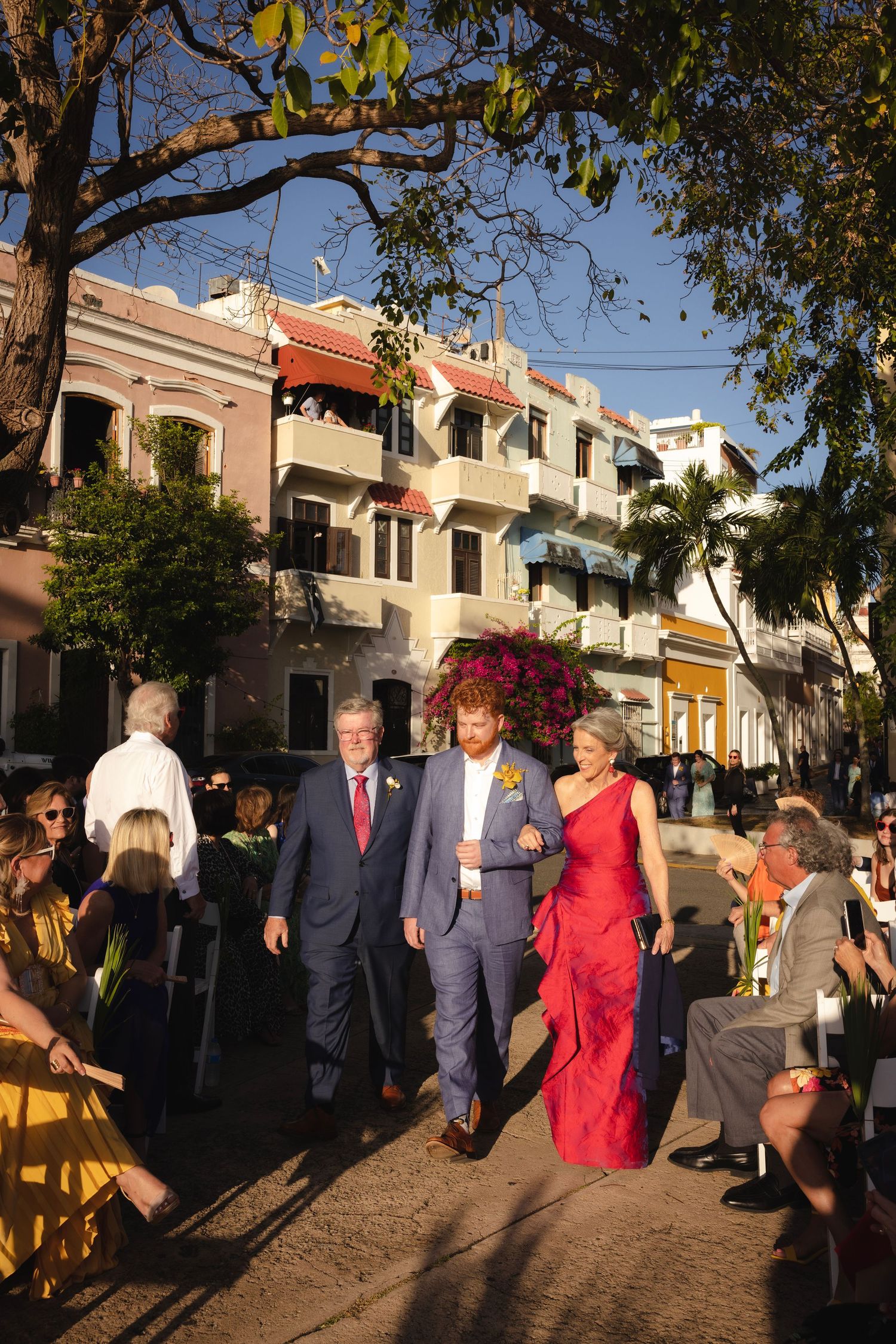 Wedding guests walking along a sunny path lined with Mediterranean style buildings.
