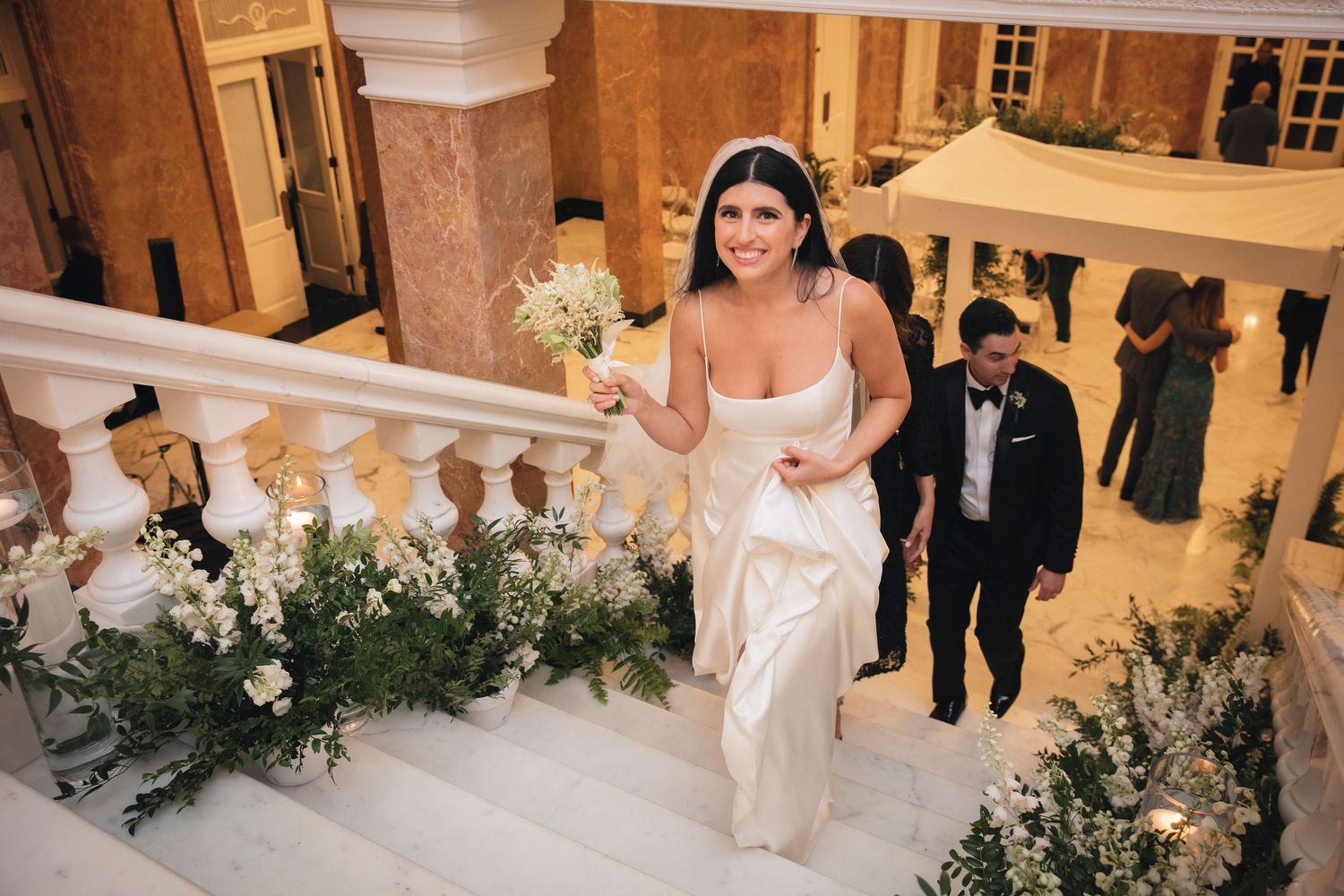 A wedding party dances together in an elegant ballroom during a reception celebration with white floral decor.