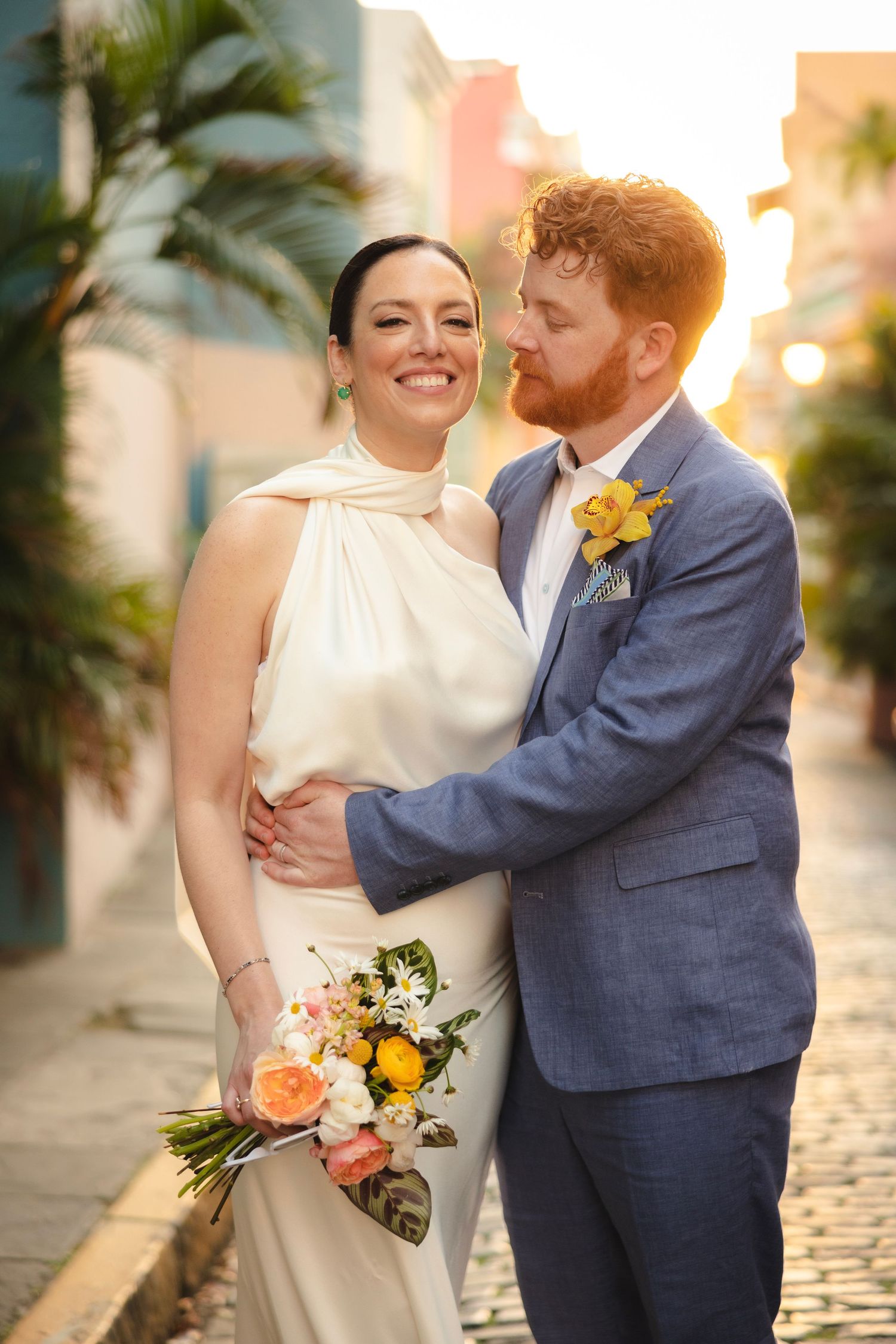 A romantic couple shares intimate moments in their wedding attire against a sunset backdrop with palm trees.