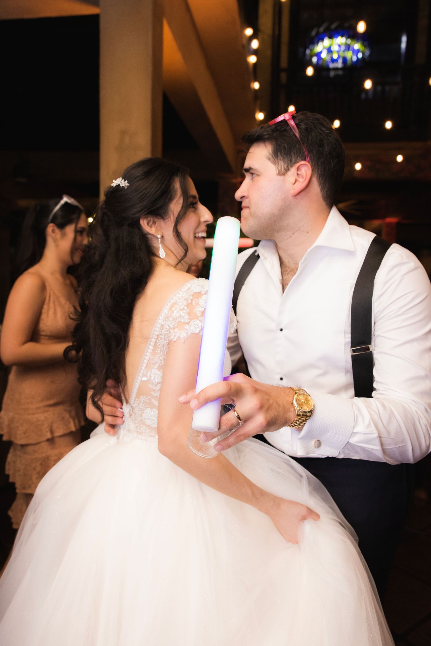 Newlyweds share a romantic dance moment under dimly lit string lights at their wedding reception.